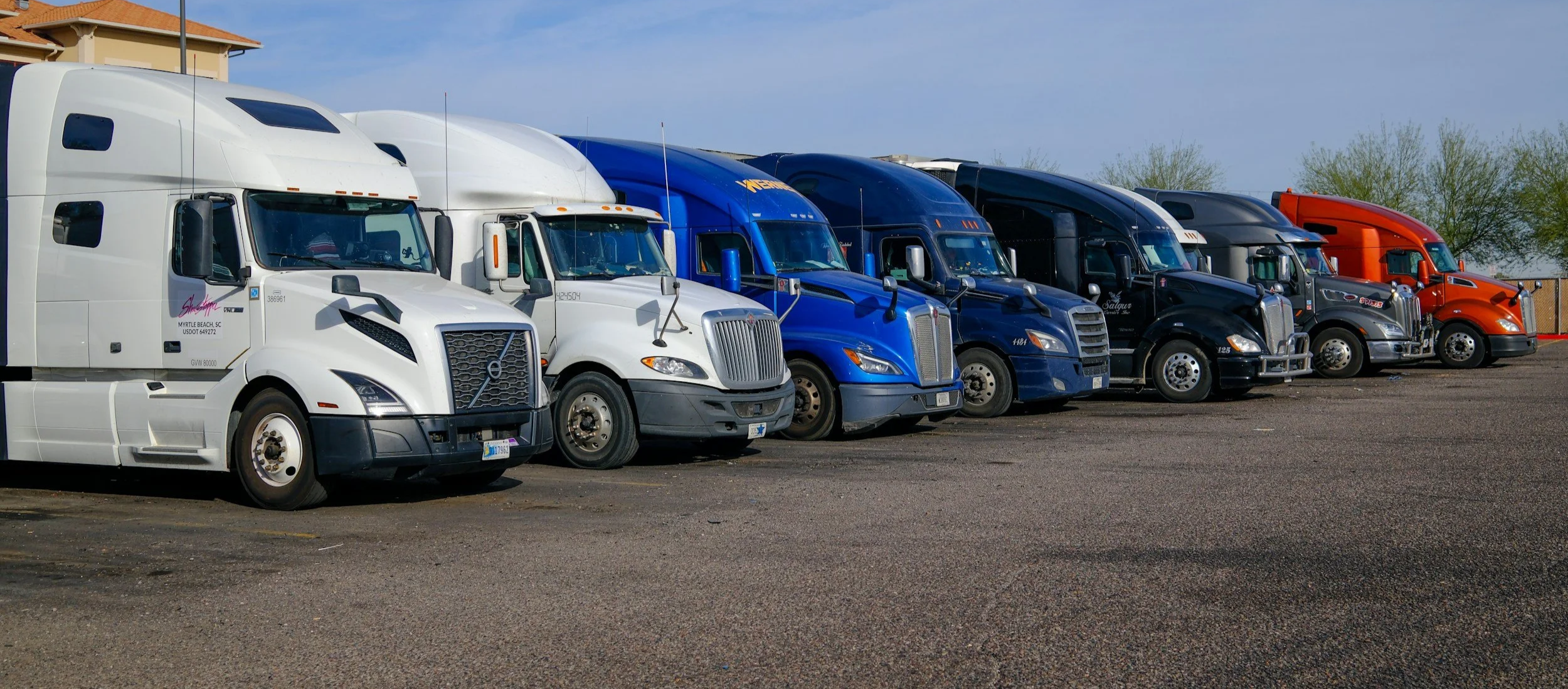 Lineup of semi-trucks parked on asphalt in a lot.