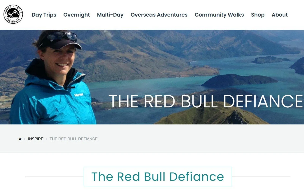 A person in a blue jacket and black cap smiling in front of a lakeside and mountain landscape with a website header for Women Want Adventure, featuring menu options for day trips, overnight, multi-day, overseas adventures, community walks, shop, and