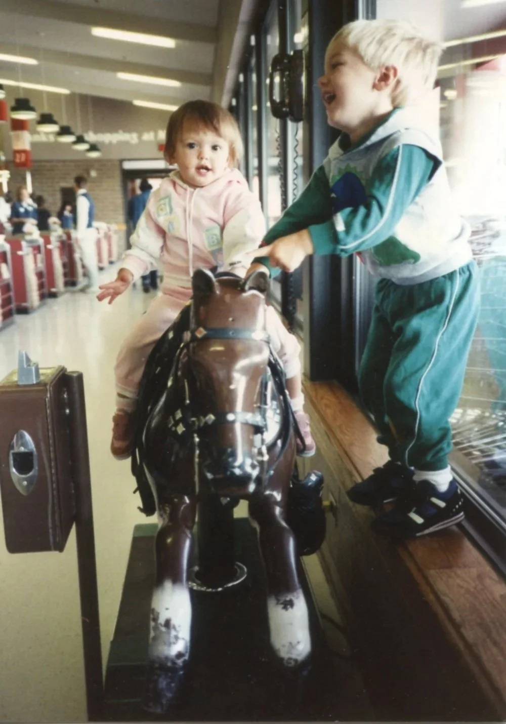 Me as a very young toddler riding the mechanical Sandy horse ride at the grocery store. My brother stands on a ledge beside us, joining in the fun