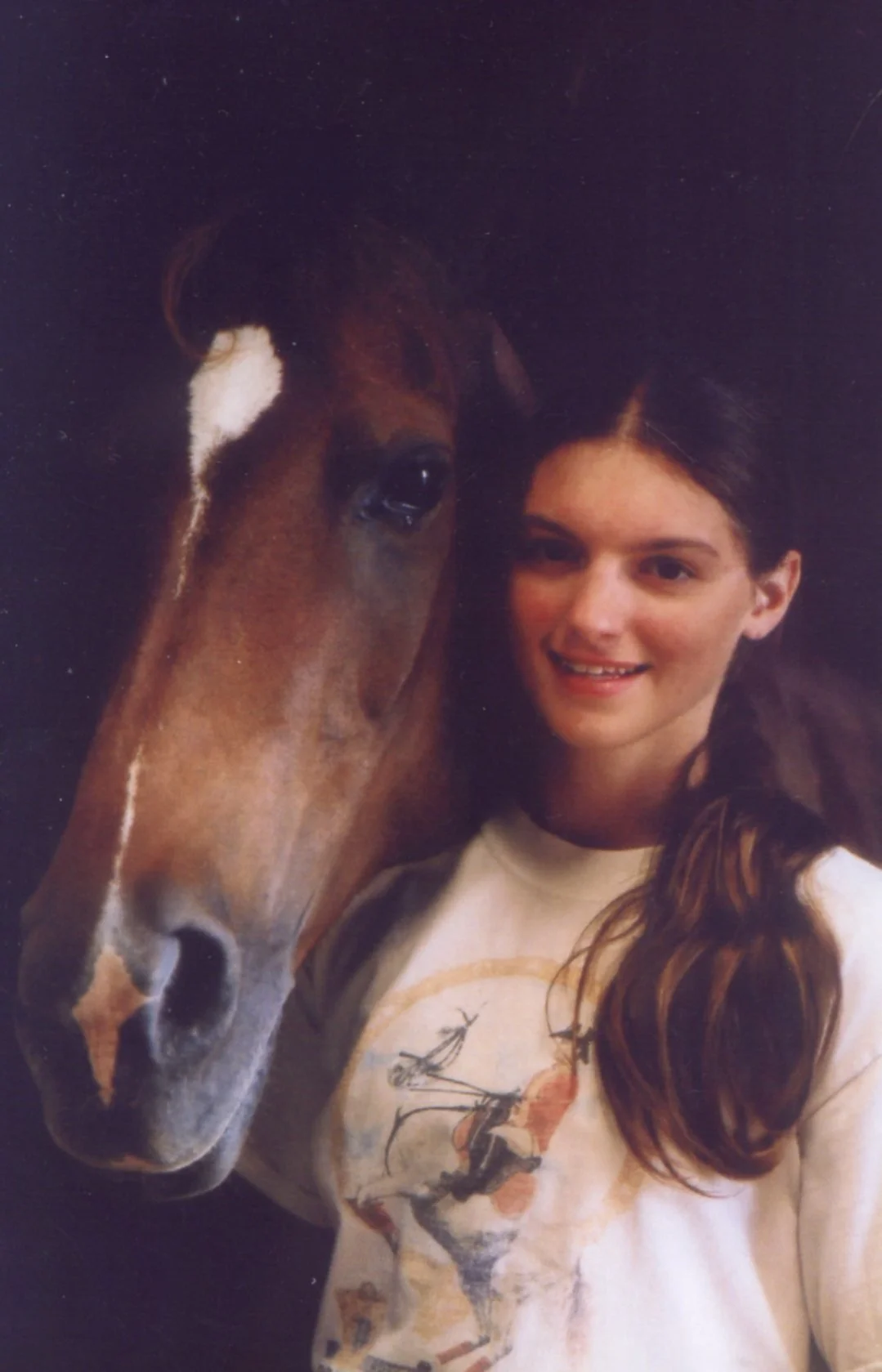 Film portrait of me as a teen with my chestnut mare. Our faces are lit by warm, gentle light that quickly recedes to blackness behind us. I have my hair in a pony tail and wear a t-shirt from a Lipizzan show