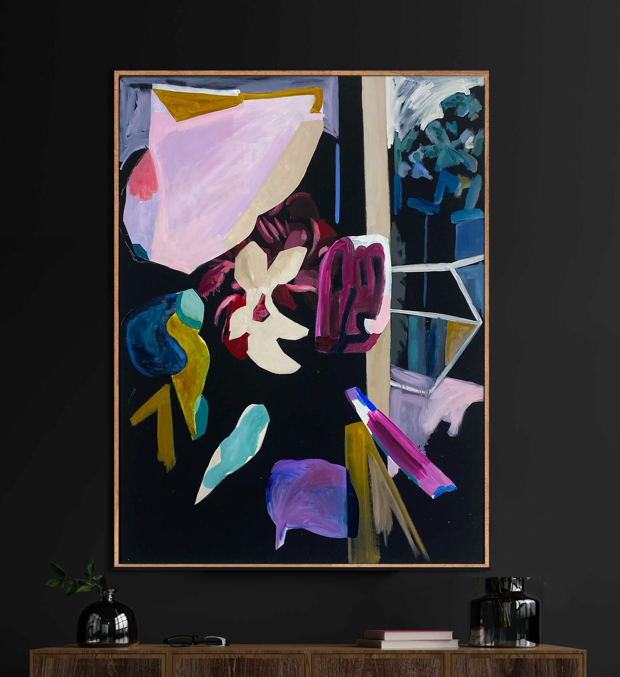 Abstract painting with various colors and shapes, including pinks, purples, blues, and yellows, hung on a black wall above a wooden console with decorative vases and books.