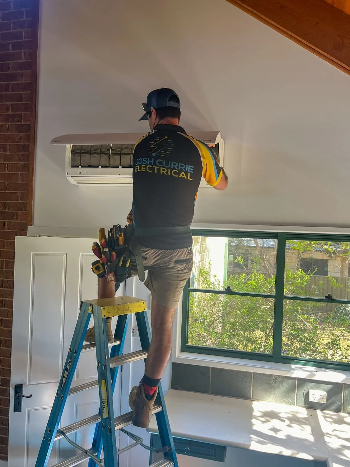 Josh servicing a split system cleaning the filter while standing on  a ladder