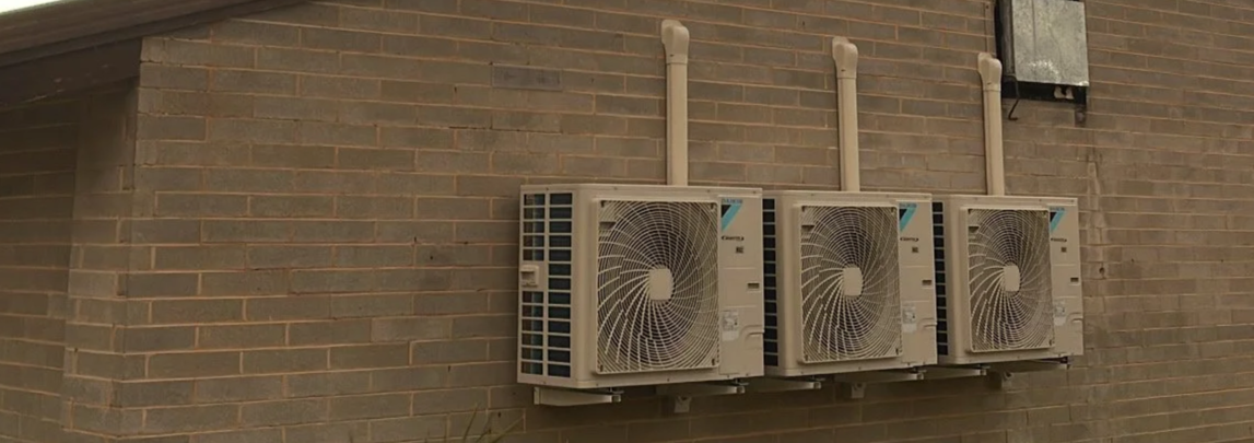 Three air conditioning units mounted on a brick wall.