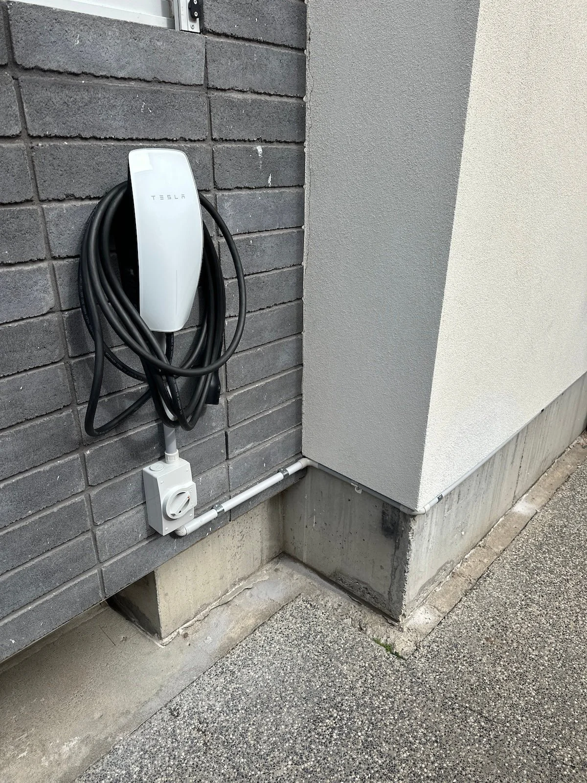 white tesla ev charget on grey brick wall with power connected