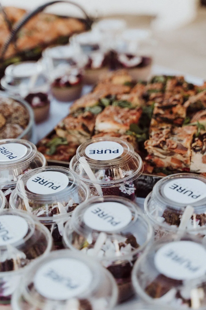 Assorted desserts and snacks on a table, including cupcakes, small jars with labels, and layered savory pastries garnished with herbs.