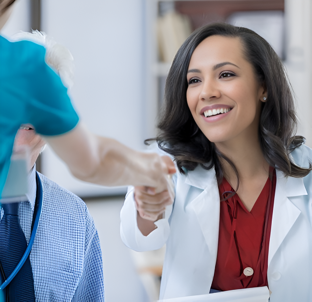 Female healthcare professional in a white coat smiling and shaking hands with a colleague in a medical office.