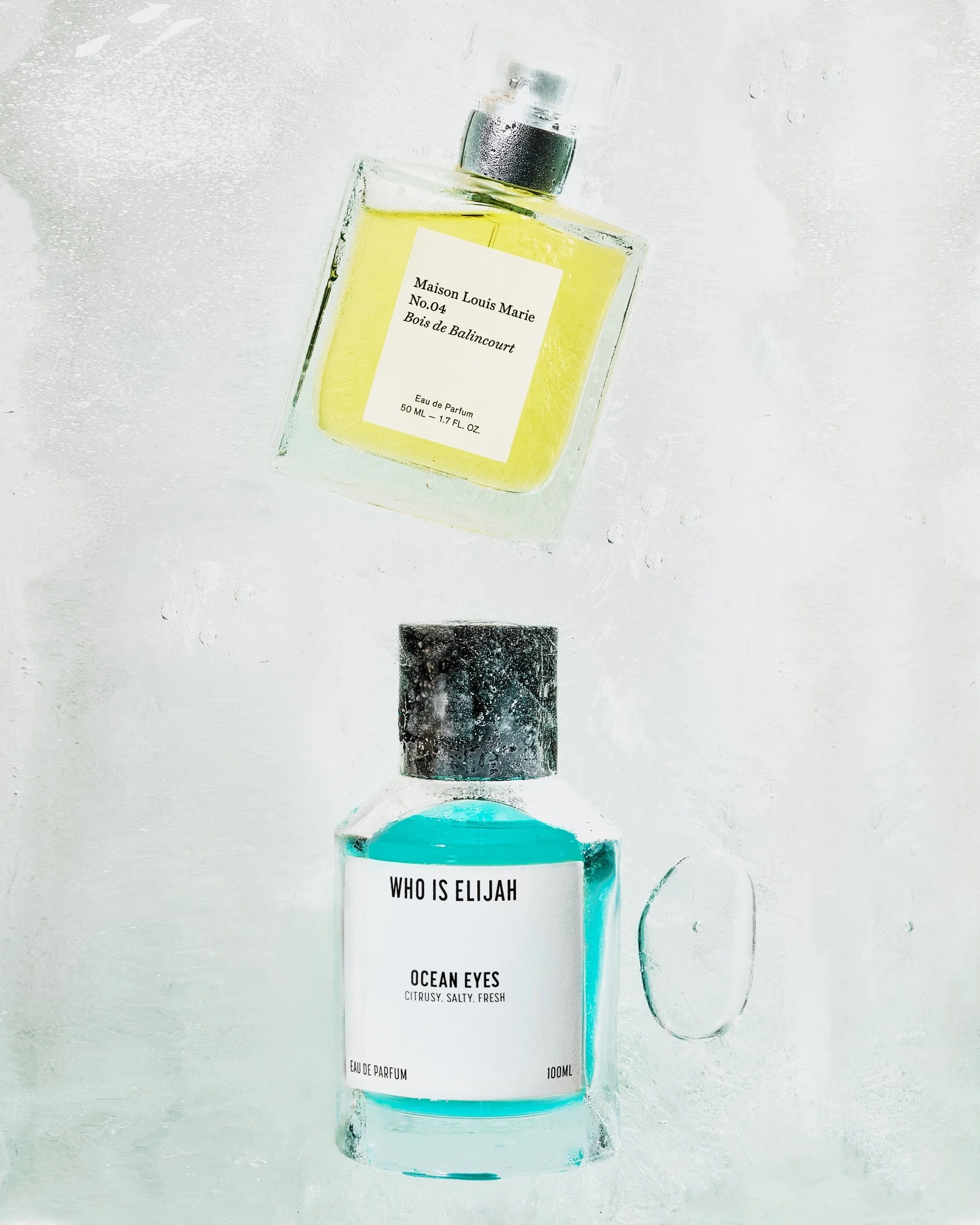 Two bottles of perfume, one with yellow liquid labeled Maison Louis Marie Bois de Balincourt, and one with blue liquid labeled Who Is Elijah Ocean Eyes.