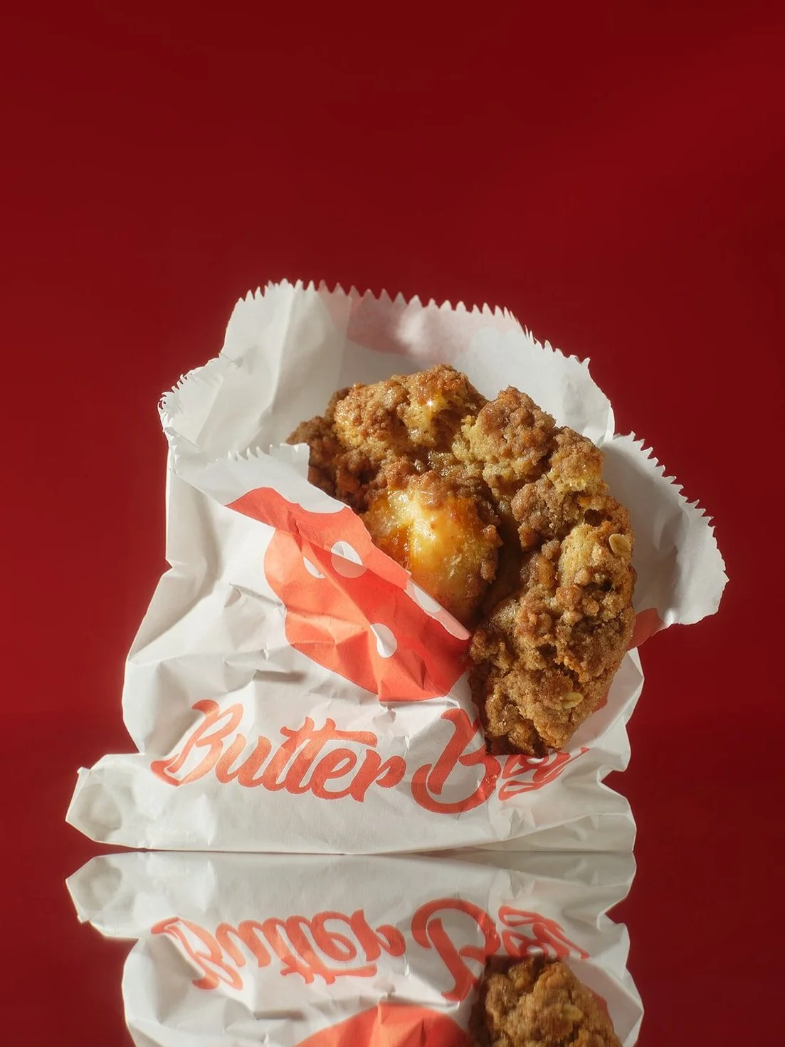 A piece of fried chicken in a white paper wrapper with orange text that says "Butter," on a red surface.