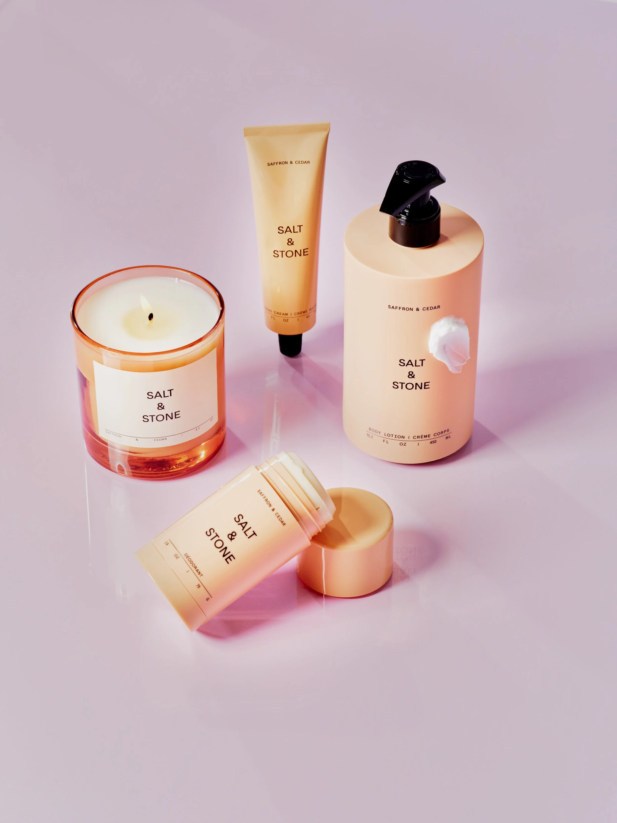 Collection of skincare products and a candle from Salt & Stone, including a lotion, spray, and deodorant on a pink surface.