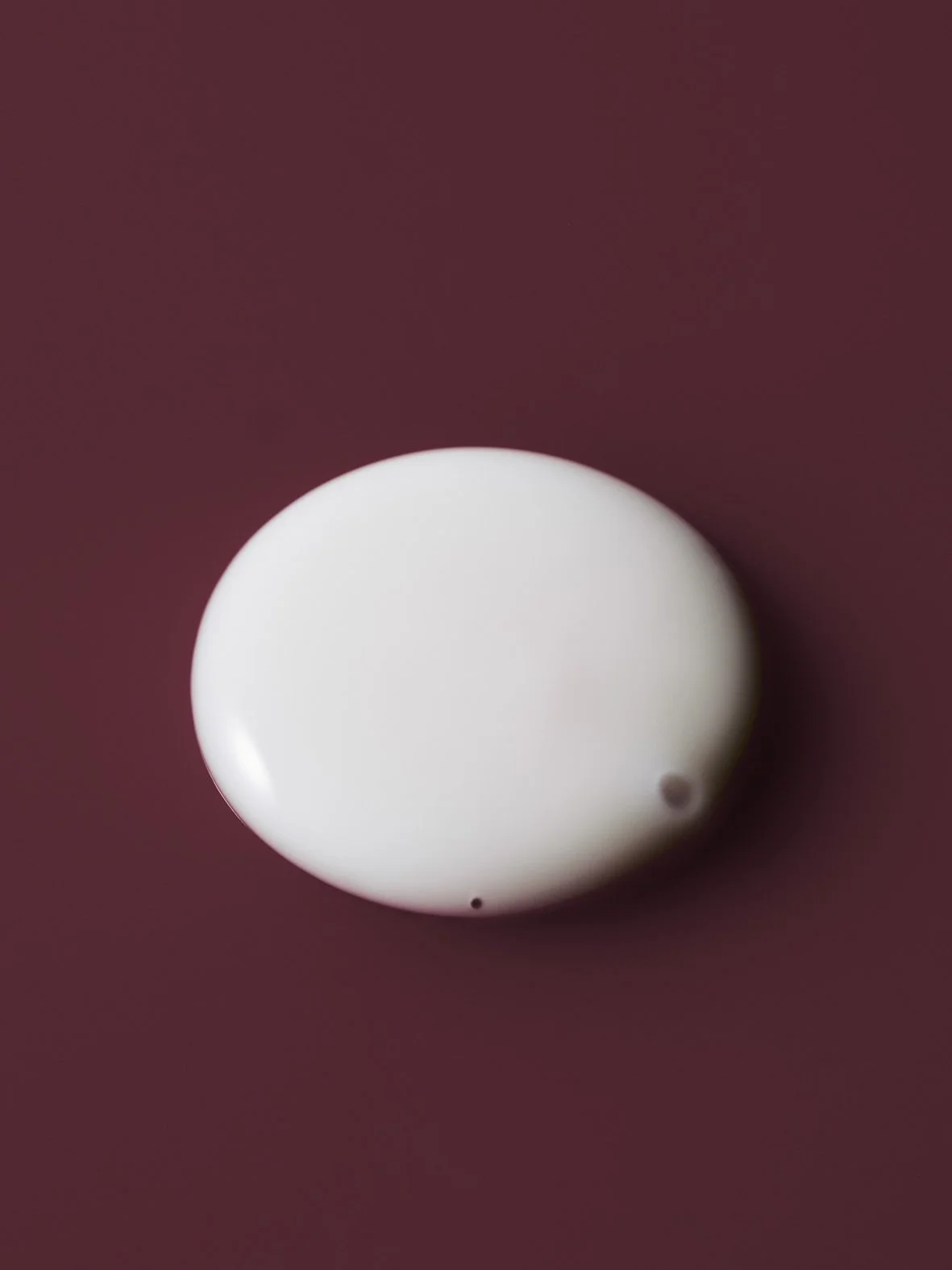A close-up of a white liquid droplet on a maroon background.