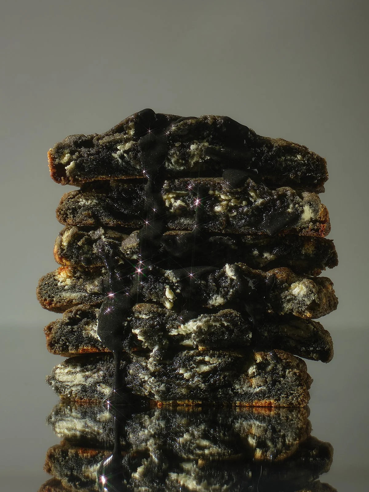 A stack of five cookies with dark chocolate and white cream, with drizzles of dark syrup, reflecting on a shiny surface.