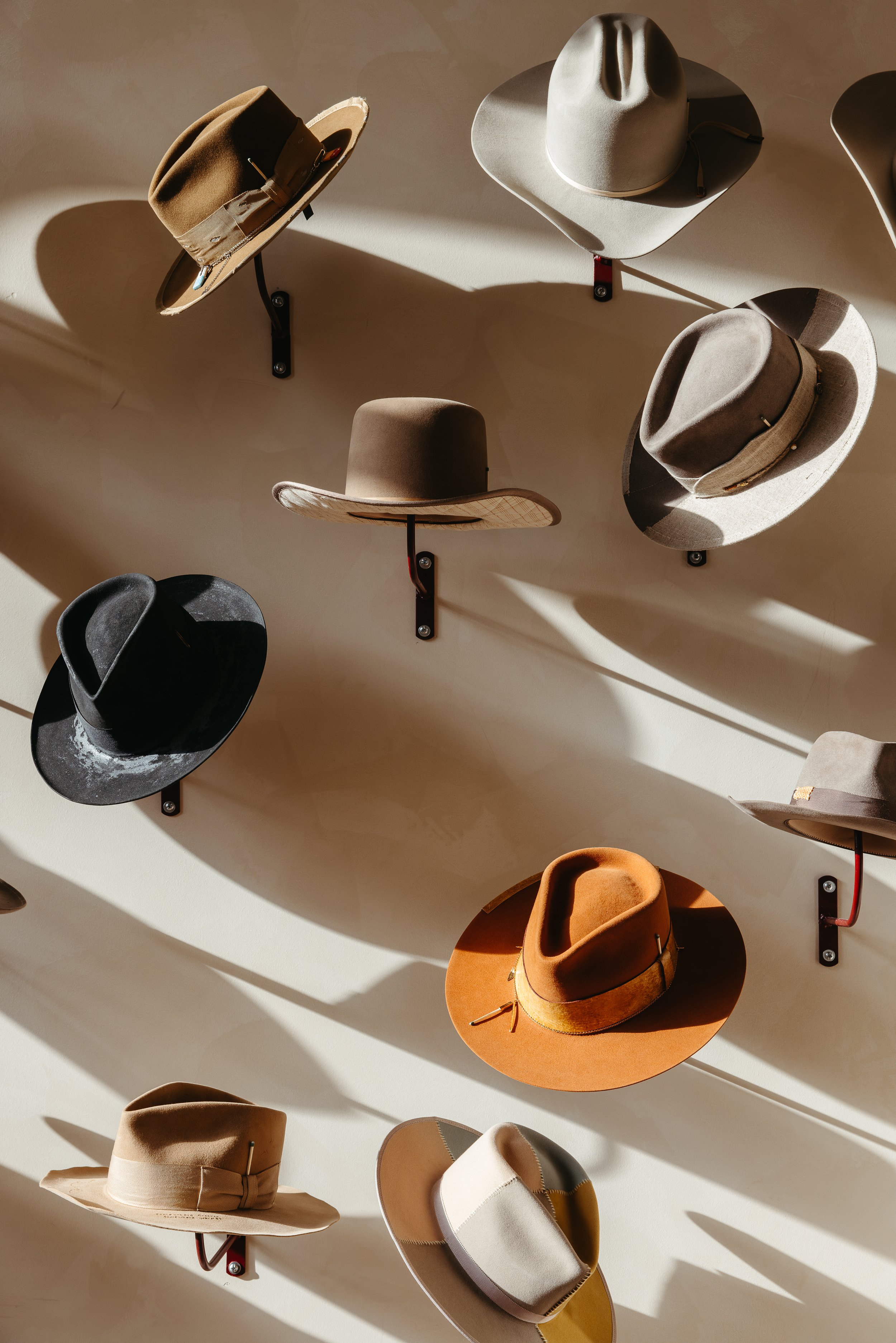 Several hats of various colors and styles mounted on a wall with shadows cast on a beige surface.