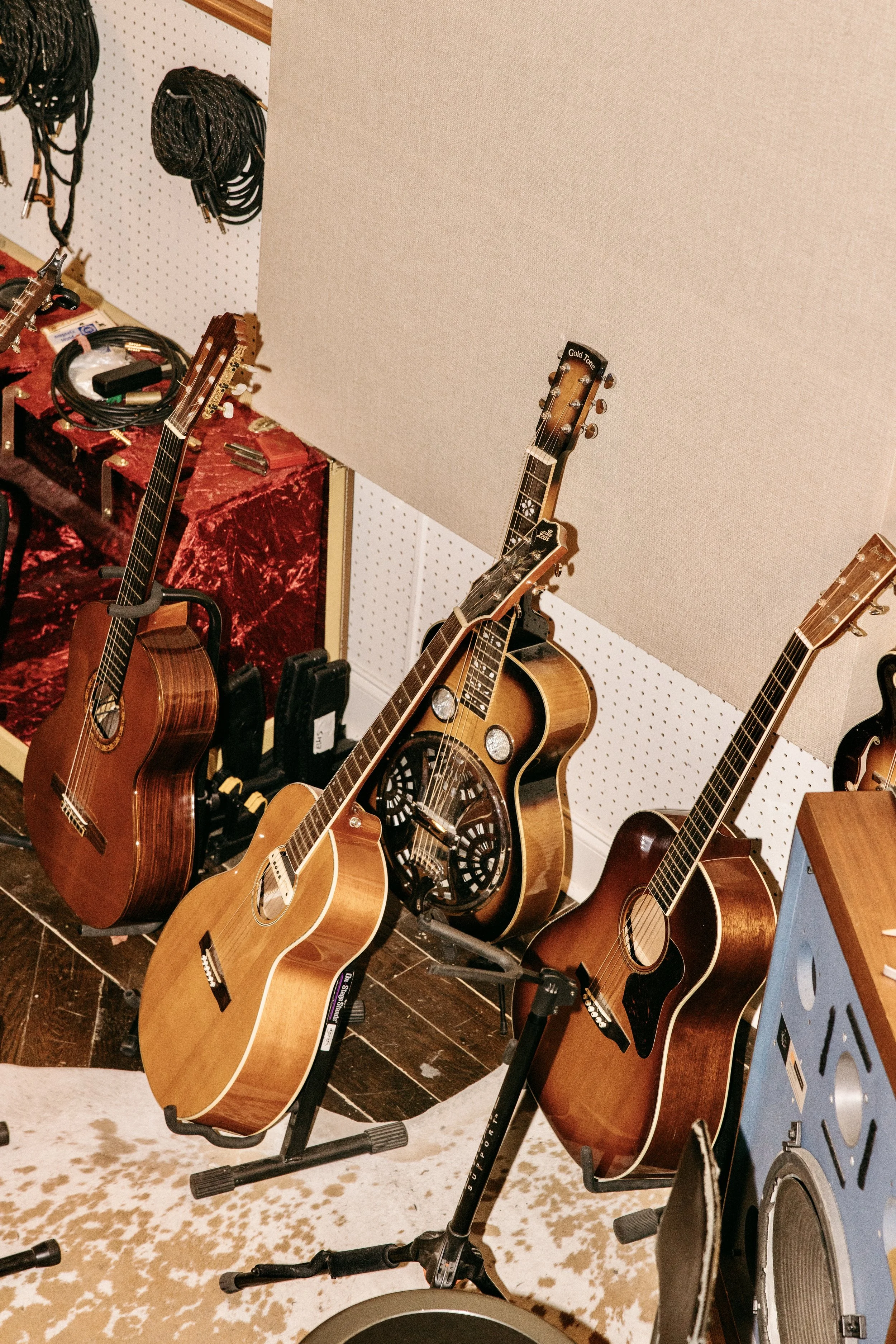 Multiple acoustic guitars on stands in a music store, with some cables and equipment nearby.