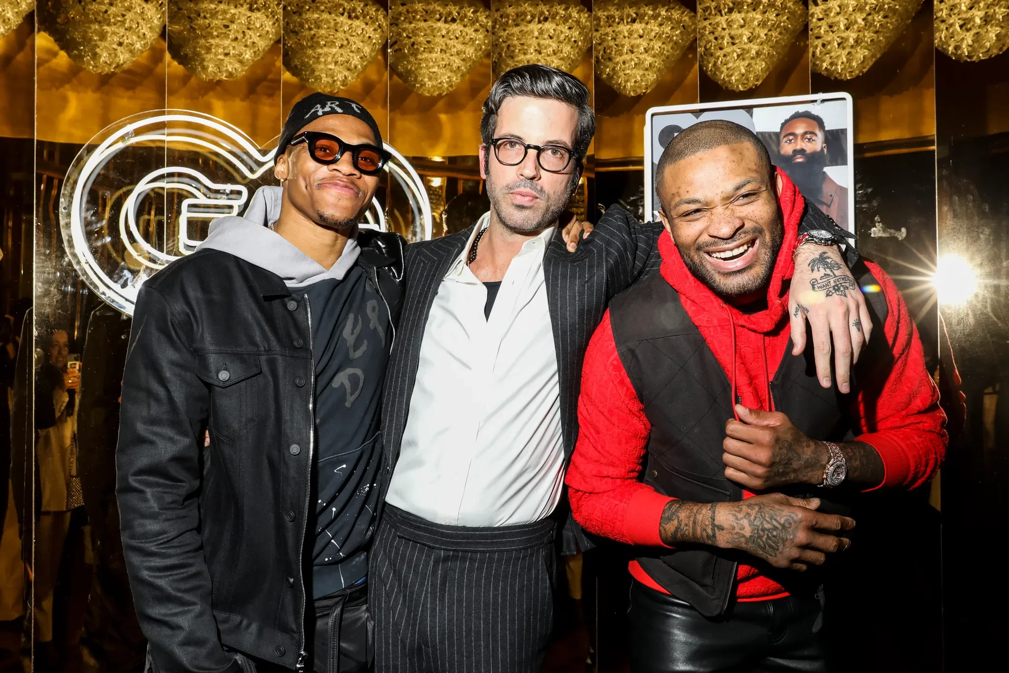 Three men posing together at an indoor event or venue, with golden decorative ceiling and a neon sign in the background, smiling and looking at the camera.