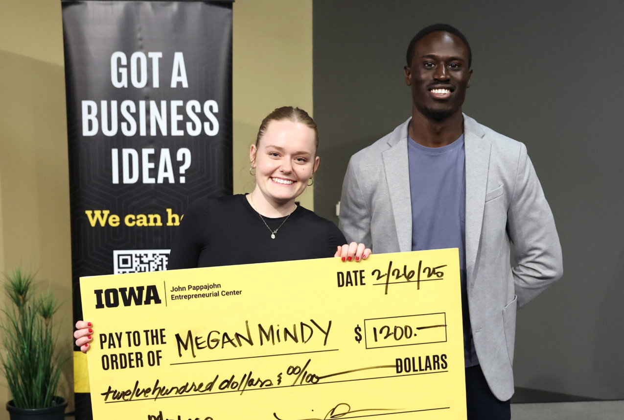 Commonground founder, Megan Mindy, stands next to an individual while she holds a reward check of $1200.