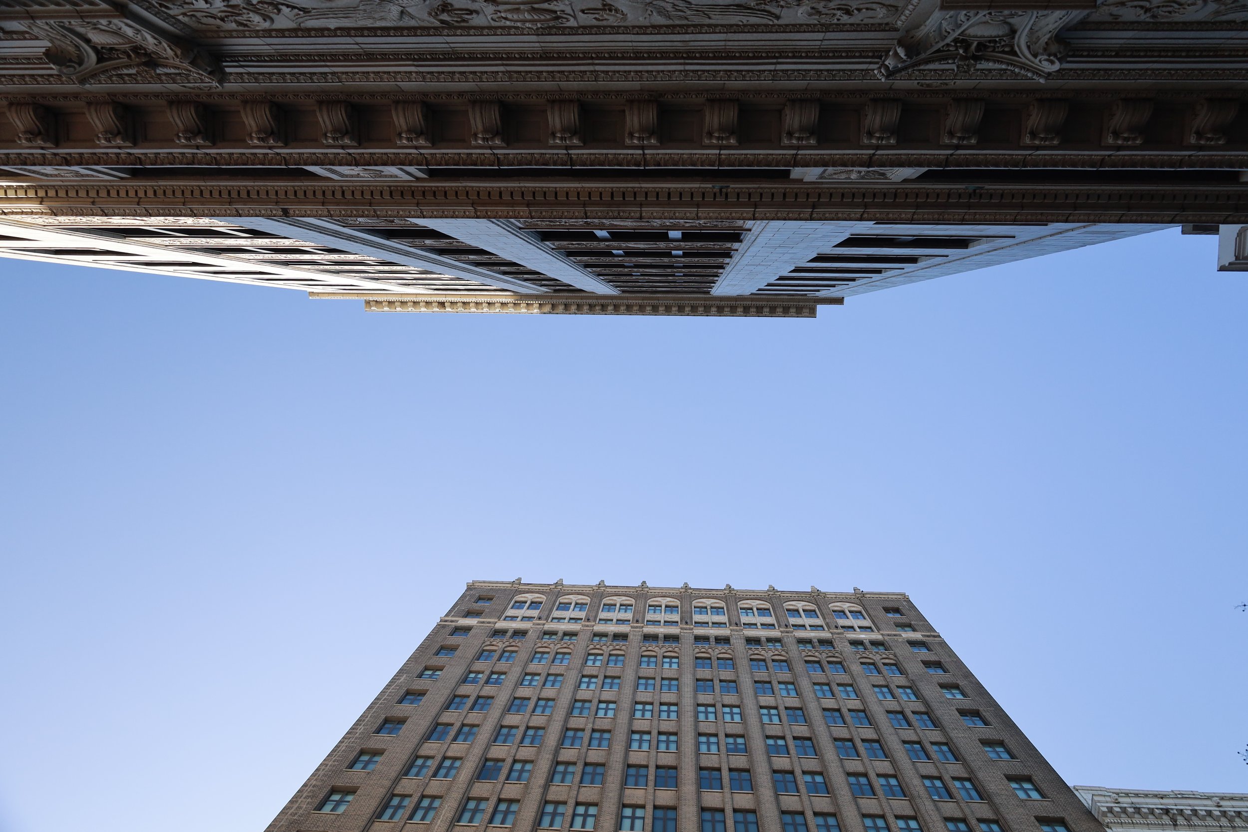 Upward view of tall buildings in a city, with blue sky in the background.