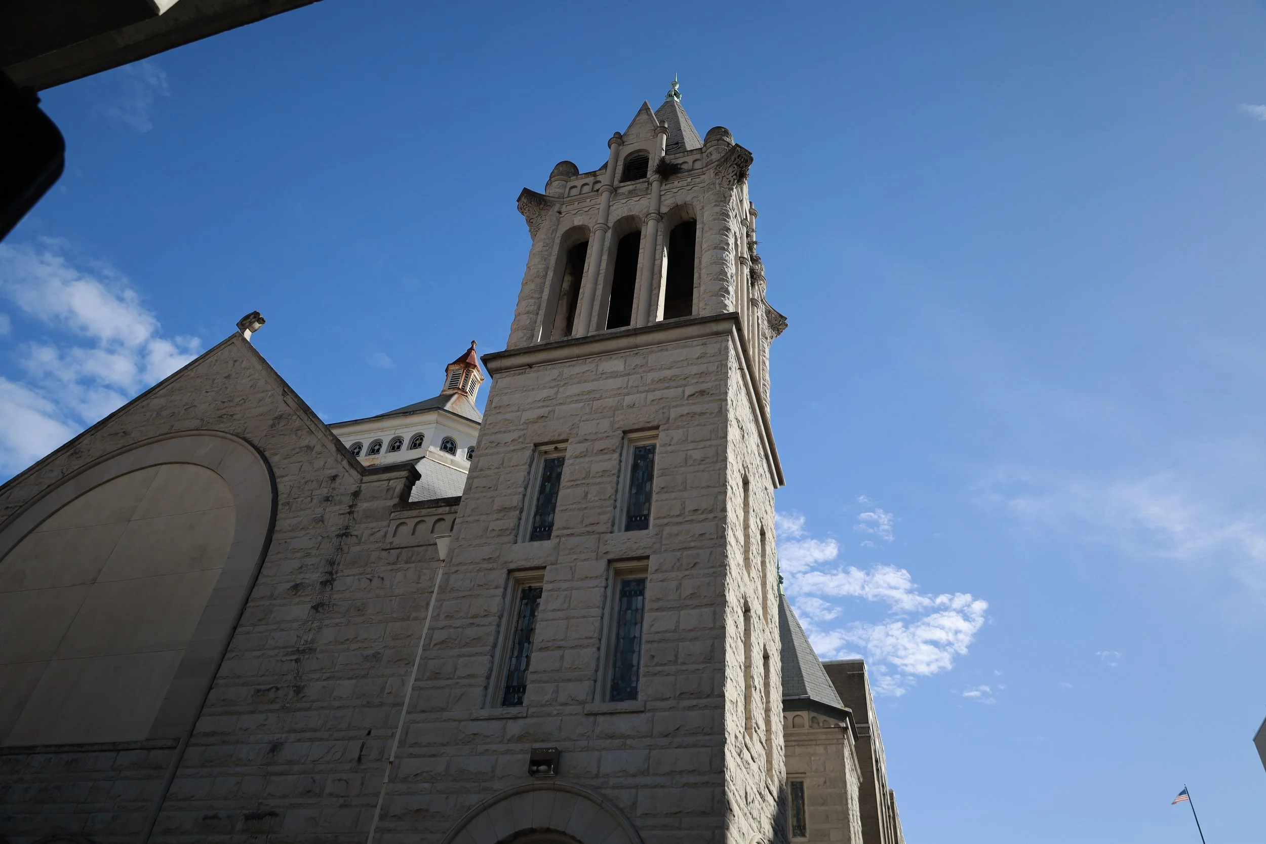 Low-angle view of a historic stone church with a tall steeple against a blue sky.