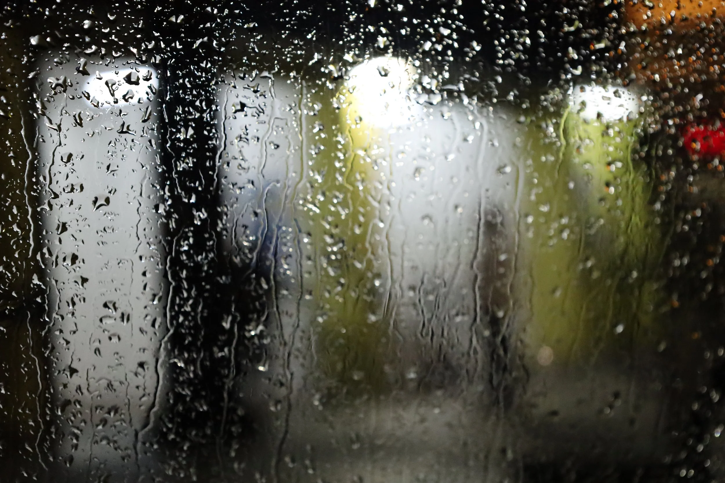 Rain droplets on a window with blurred outdoor scenery in the background.