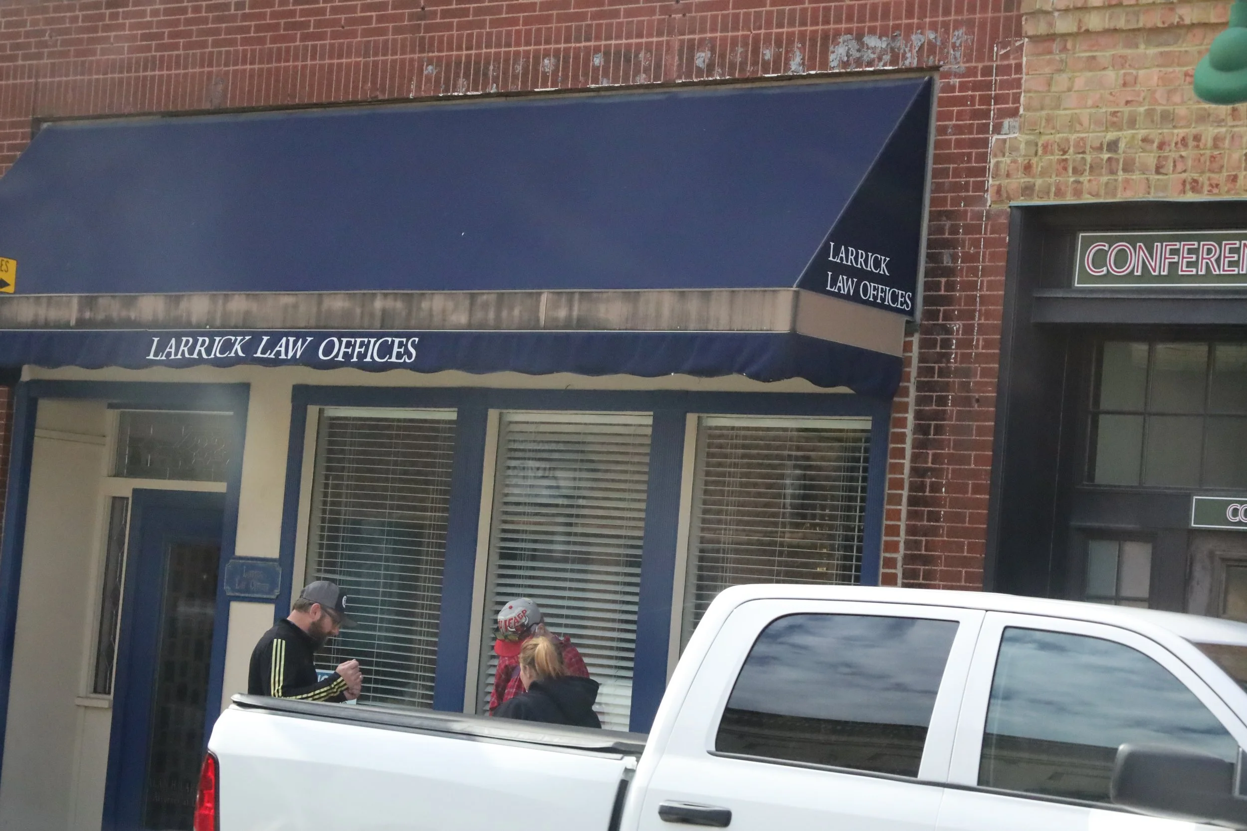 Street view of Larrick Law Offices with a blue awning, windows with blinds, and people standing outside near a white truck.