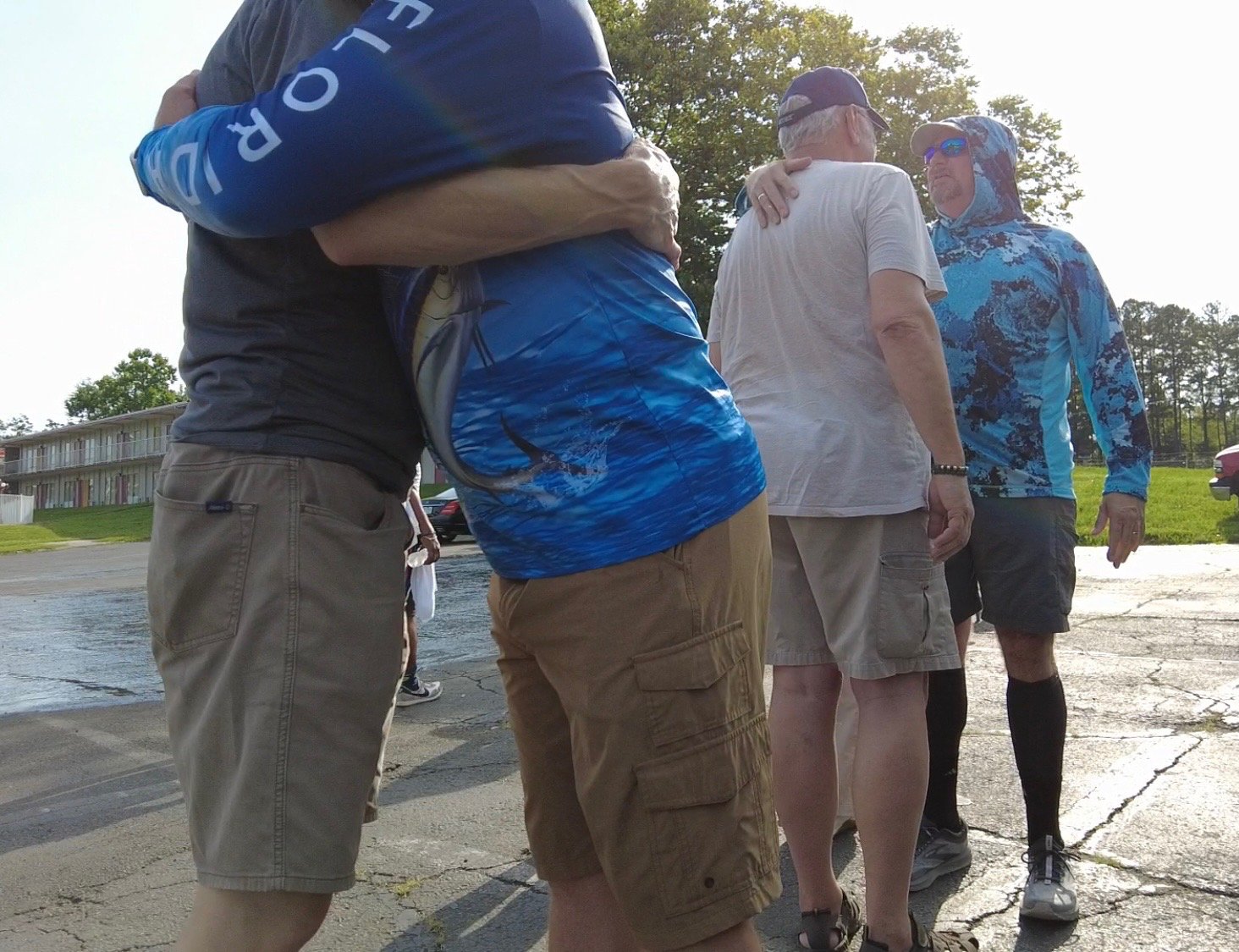Group of casually dressed people standing outdoors in bright sunlight and talking to each other.