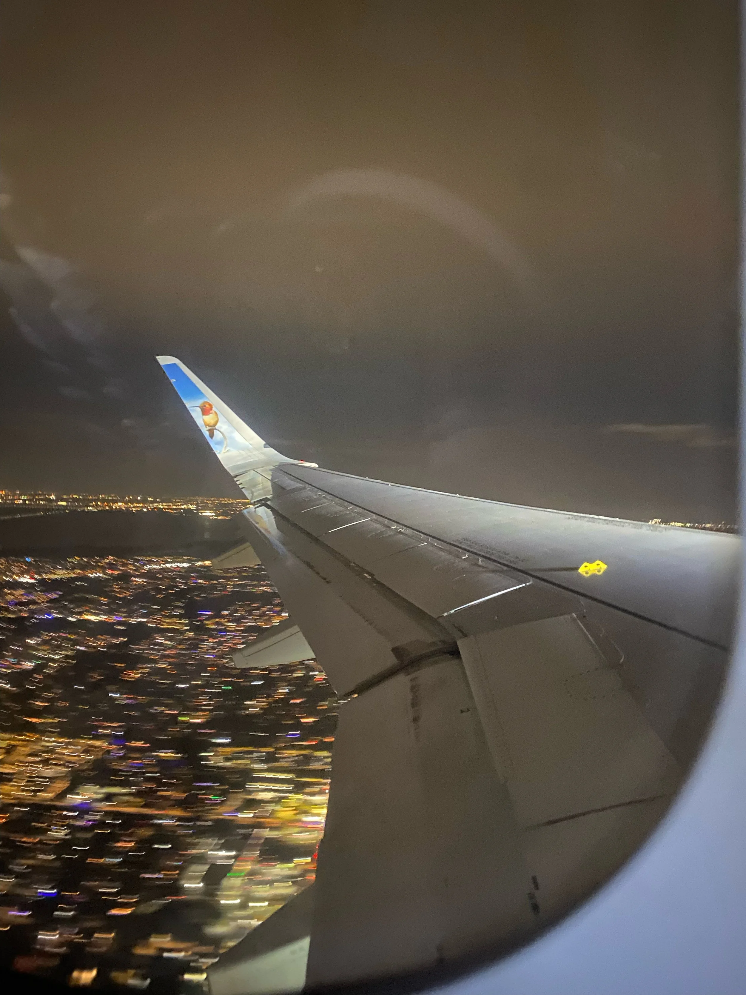 View of an airplane wing at night with city lights below and cloudy sky overhead.