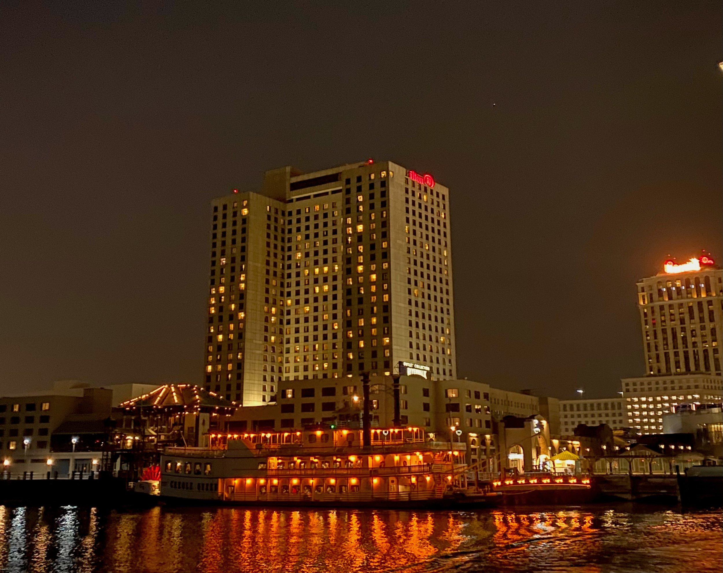 Nighttime cityscape with illuminated tall hotel and boat docked on water.