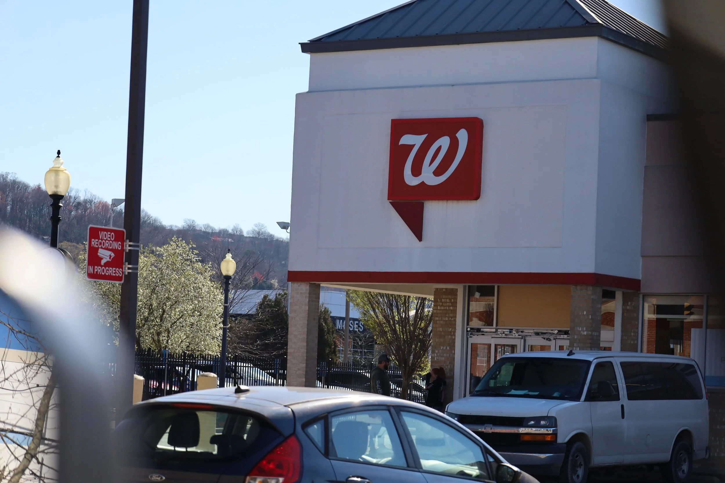A Walgreens store with its red and white logo on the building, cars parked outside, with people praying outside.