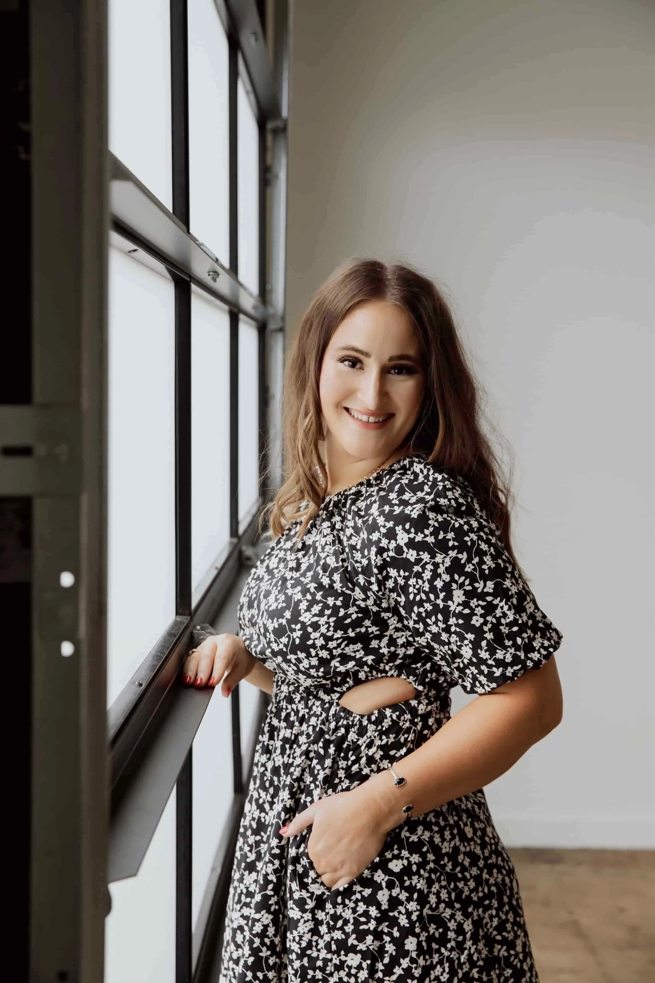 Founder of Own The Moment Club Stephanie Lindsey posing and smiling in a black and white floral dress. Stephanie helps therapists and business owners build successful businesses