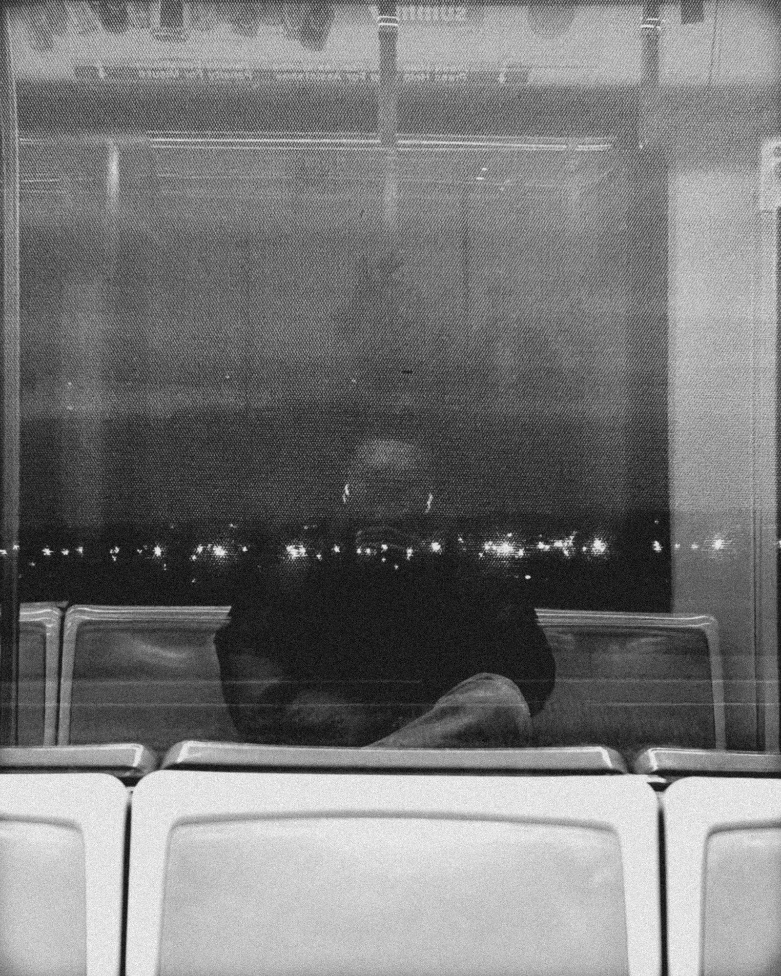 Black and white self portrait of Malik Adegbola reflected in a train window at night.