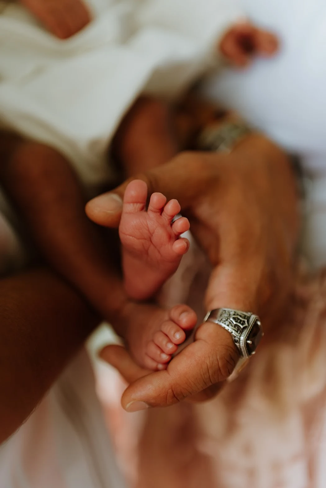 Close-up of a newborn baby's tiny hand holding an adult's finger, with both showing skin tones and the adult wearing a silver ring and bracelet.