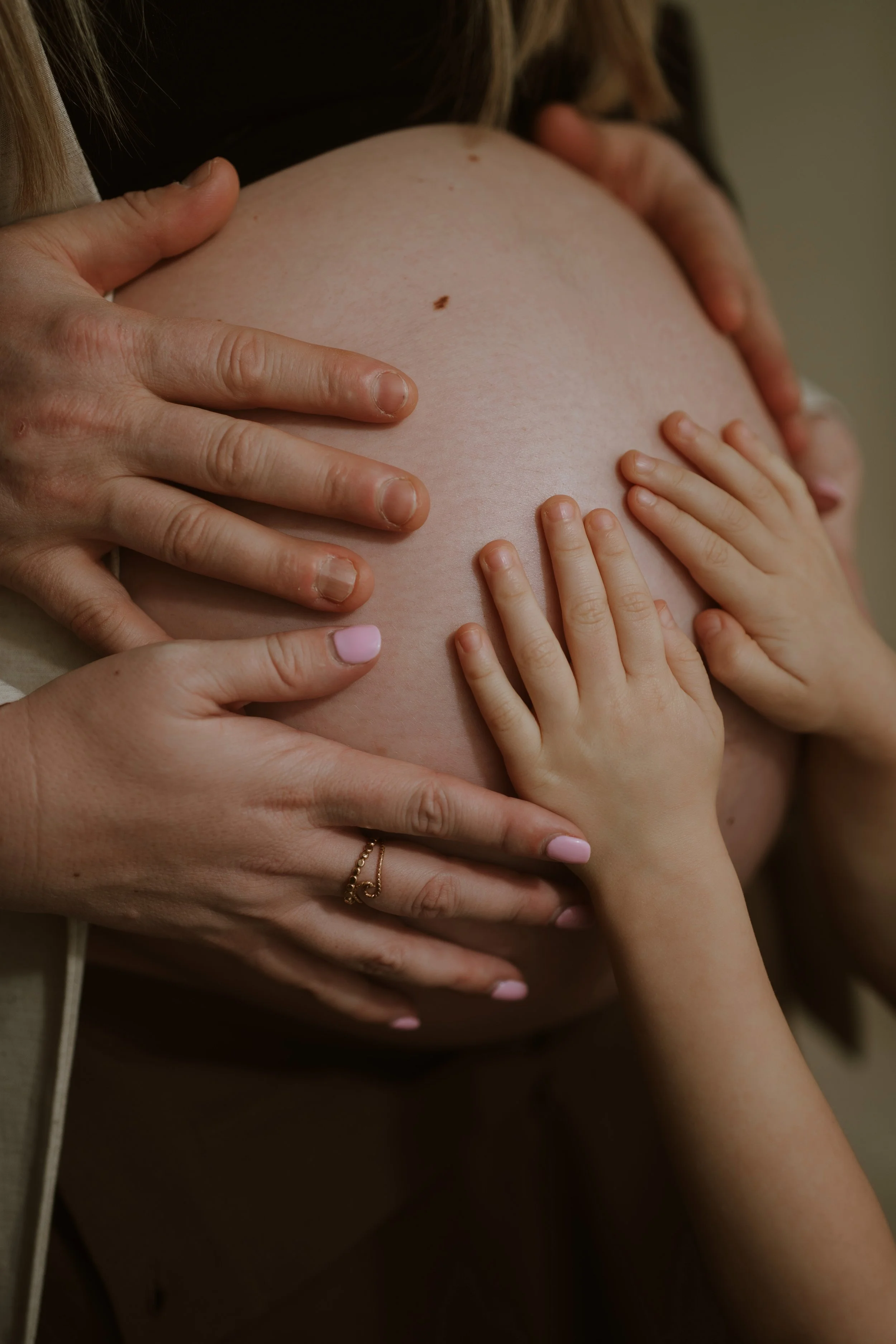 Close-up of a pregnant woman's belly being touched by multiple hands, including those of children and adults, in a caring manner.