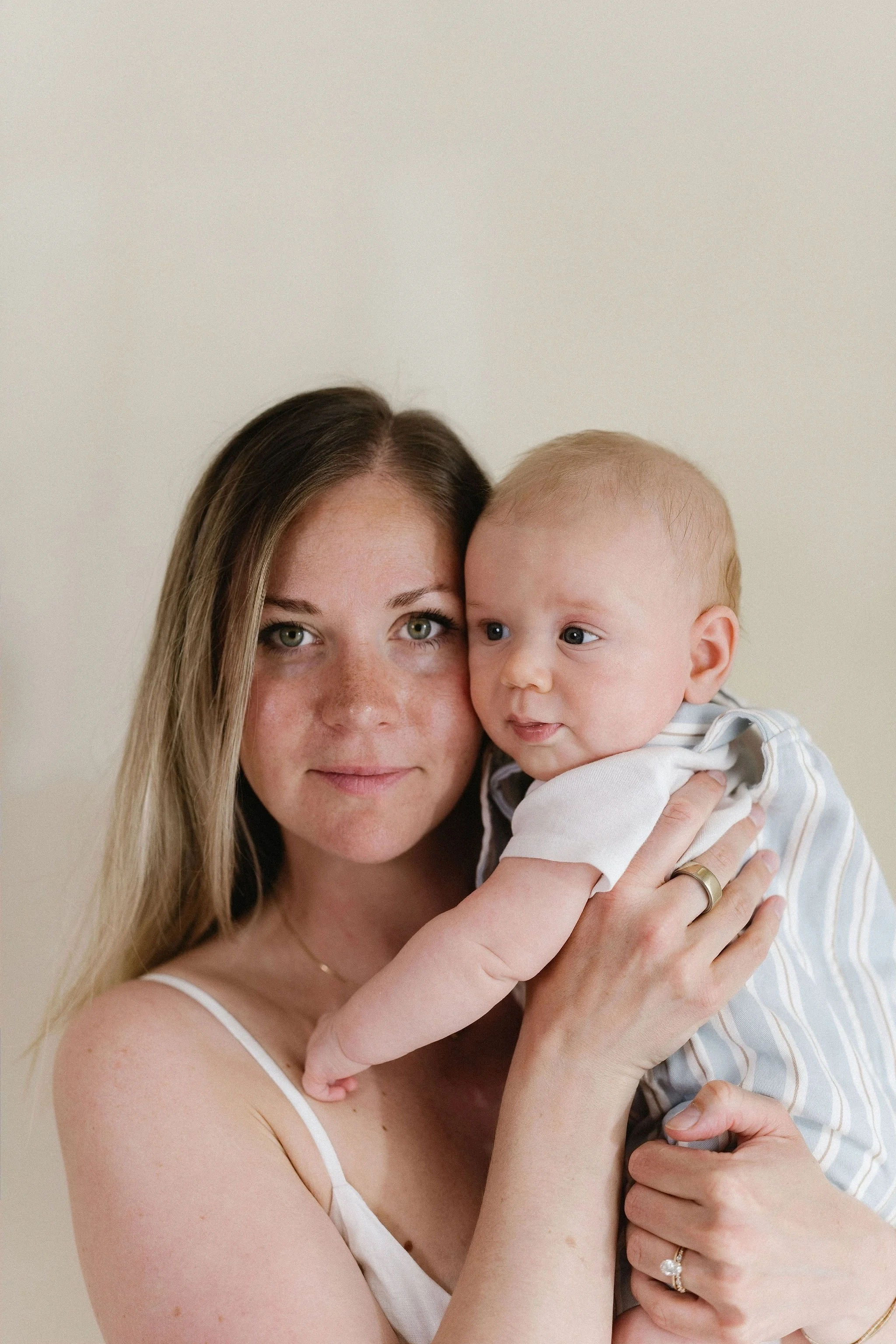 A woman with long blonde hair holding a young boy with blond hair, both looking at the camera against a neutral background.