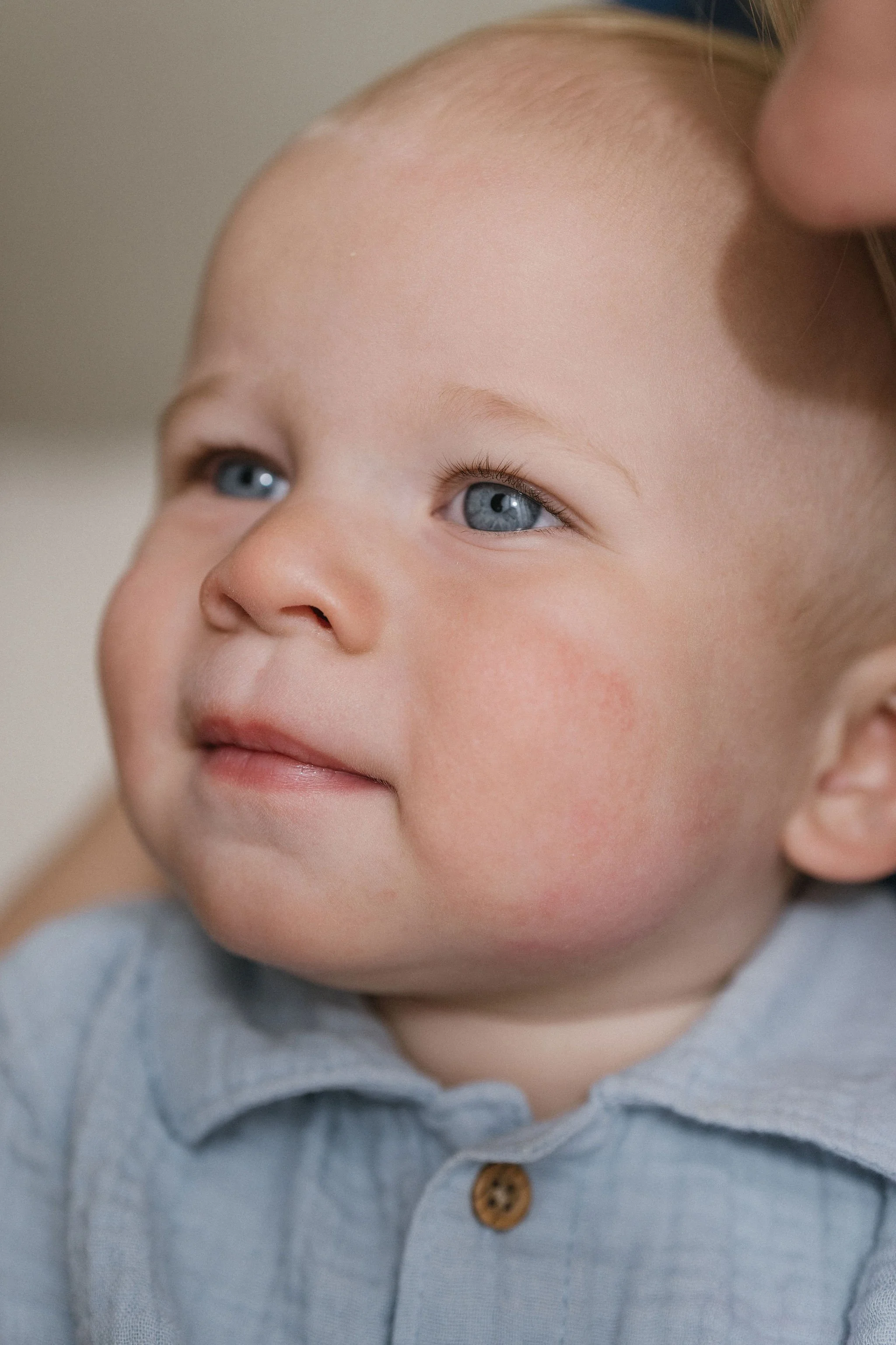 Close-up of a young child's face with light skin, blue eyes, and light blond hair, wearing a gray collared shirt.