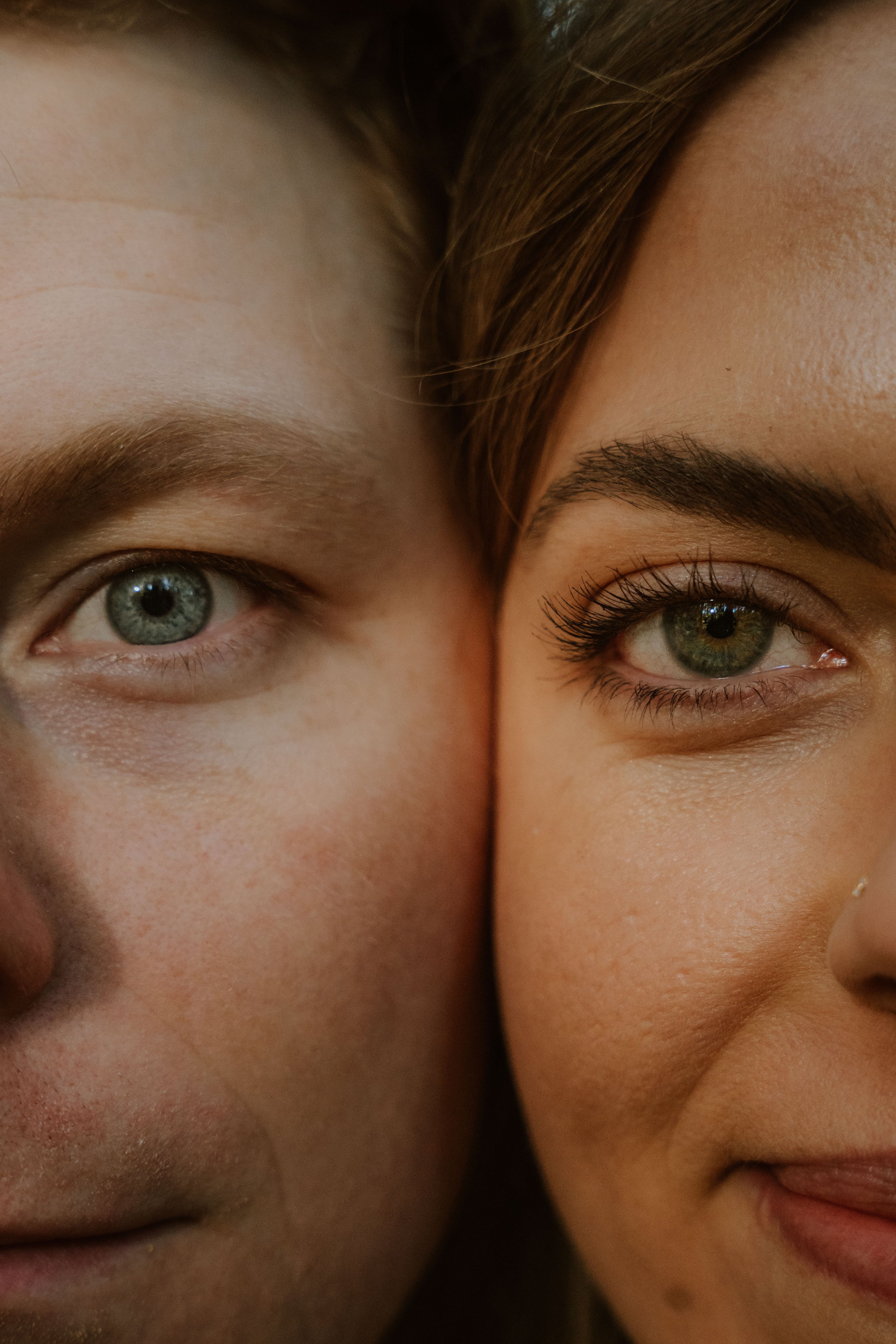 A close-up of two smiling faces with their cheeks touching, showcasing their eyes, eyebrows, and part of their noses and mouths.