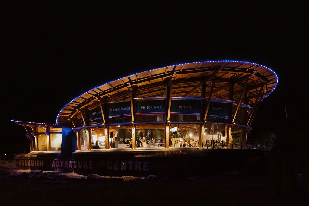 Night view of the Squamish Adventure Centre with a circular wooden structure illuminated by blue lights.