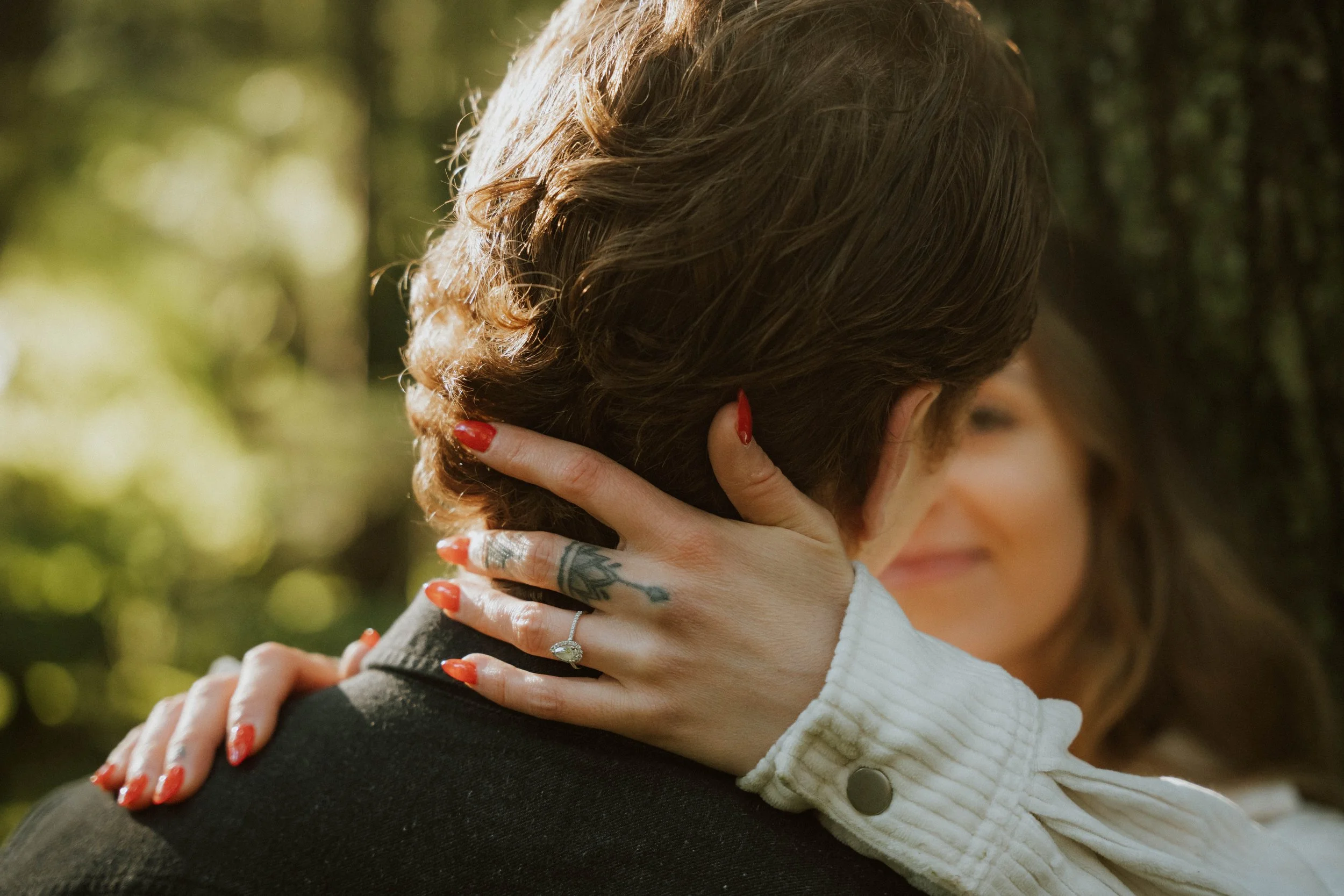 A woman with brown hair and red nails hugging someone outdoors in sunlight.