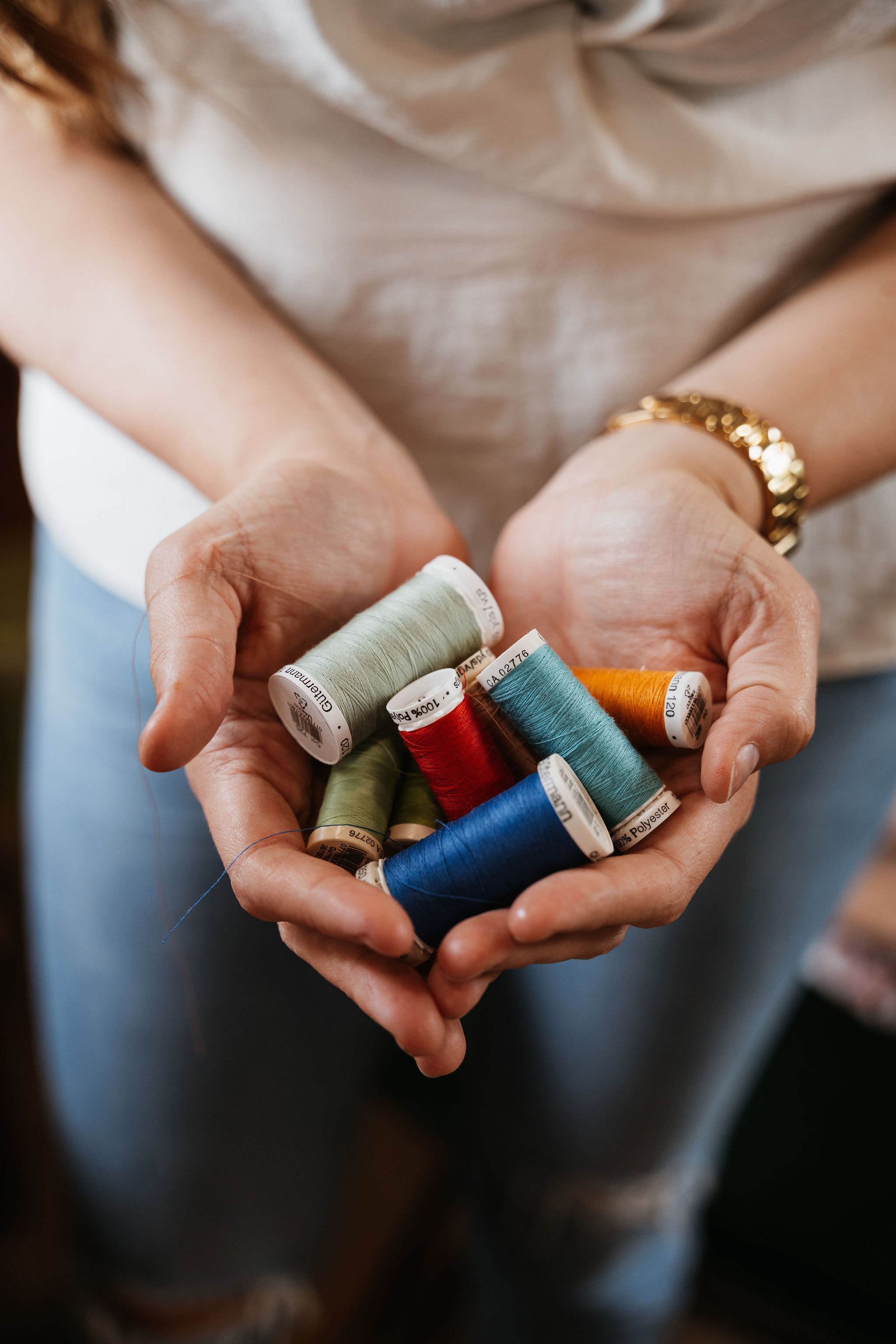 Close-up of a person's hands holding various spools of colorful sewing thread.