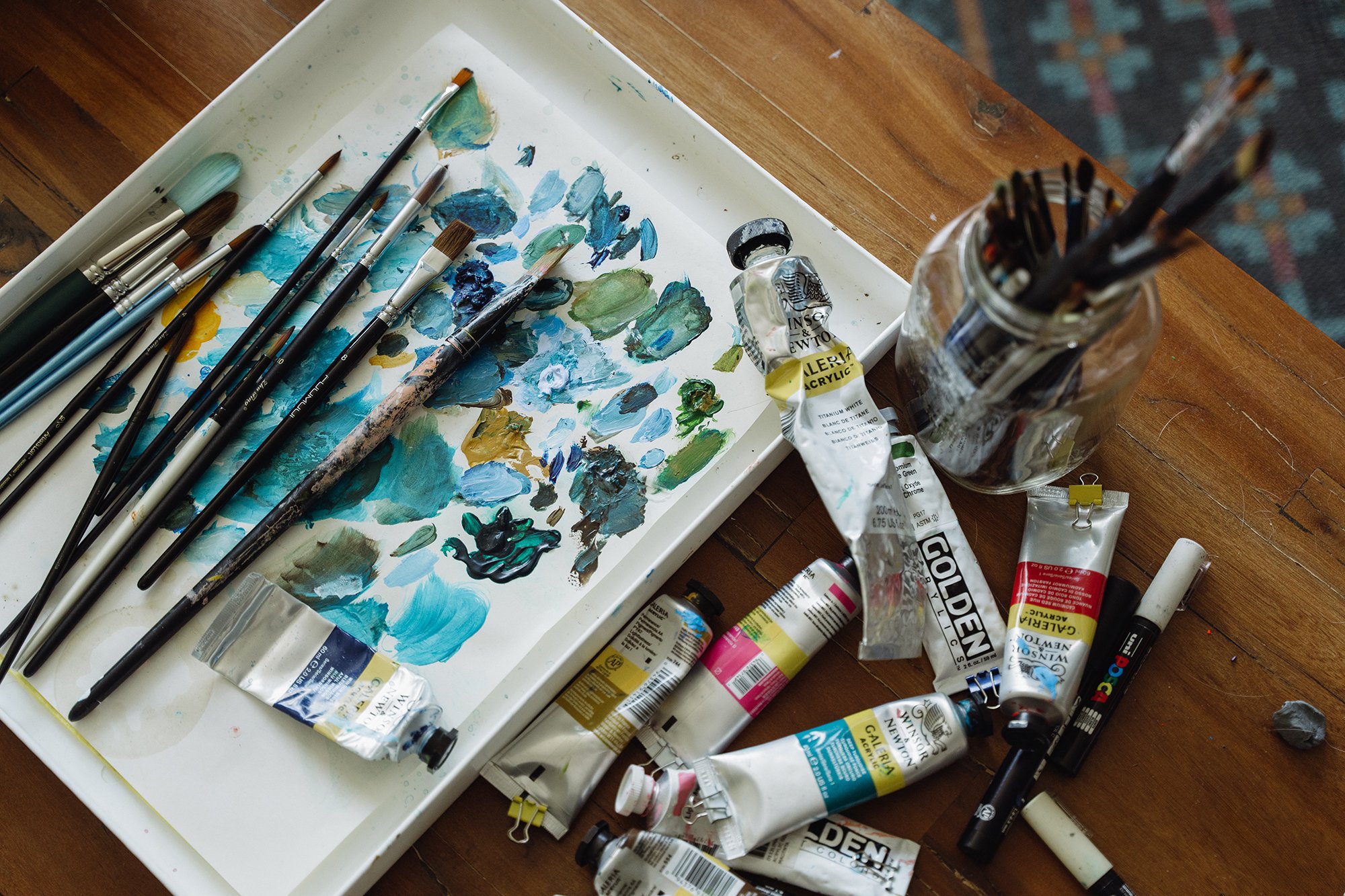 Painter's workspace with paintbrushes, tubes of acrylic paint, and a paint palette on a wooden table.