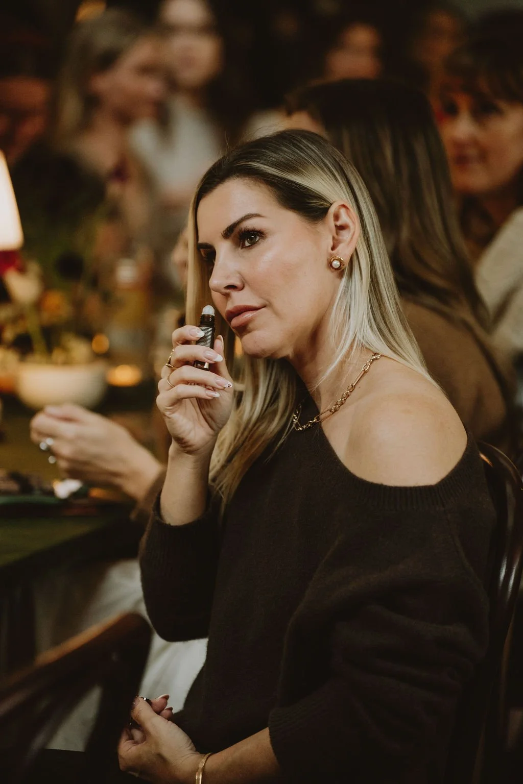 A woman with blonde hair and earrings holding a vape pen at a social gathering.