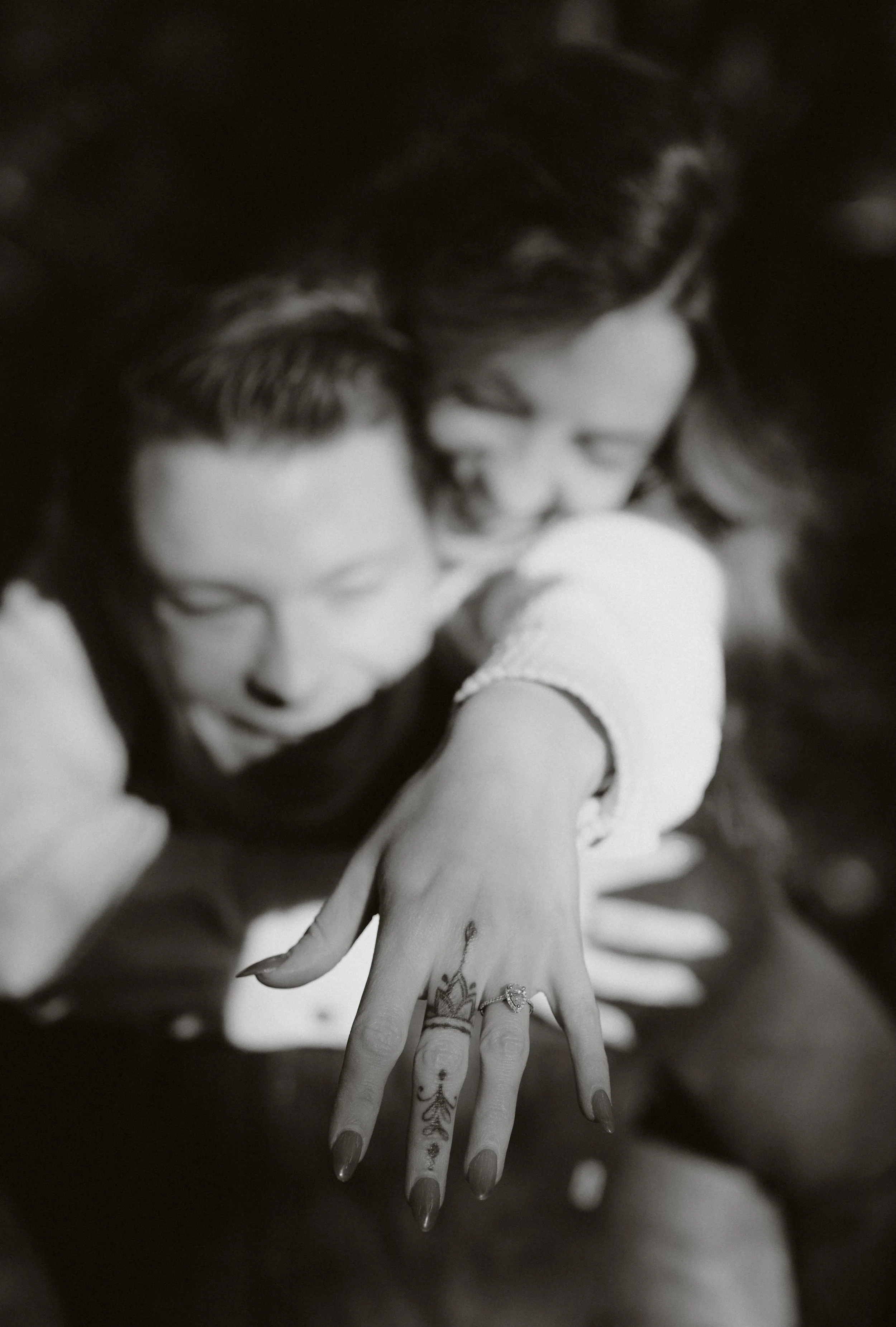 Black and white photo of two women embracing, with focus on their hands and jewelry, close-up shot.