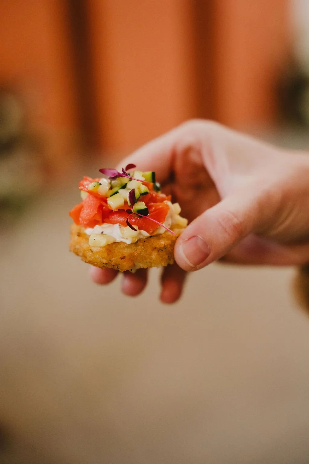 A hand holding a piece of fried food topped with chopped vegetables and microgreens.