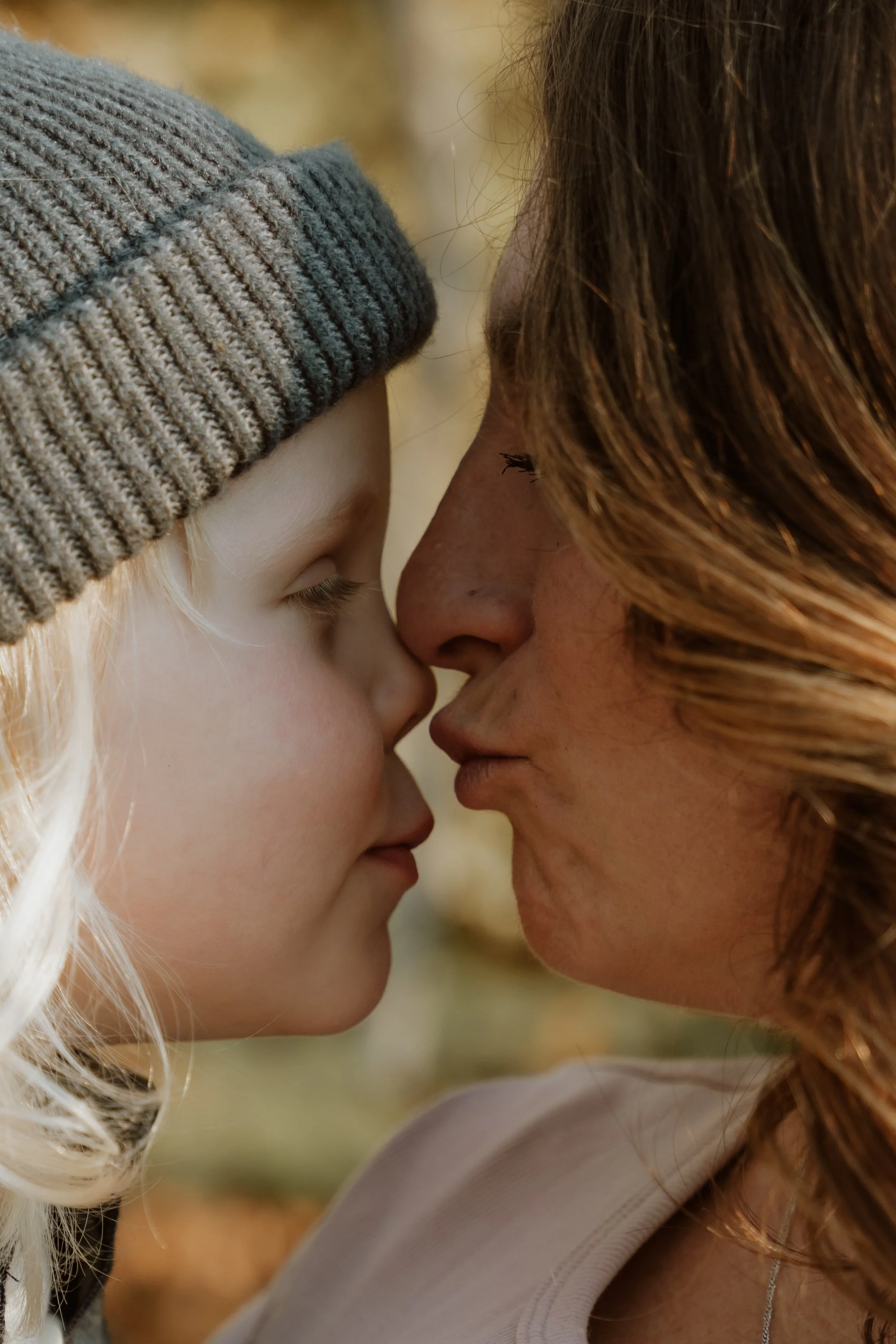 A close-up of a young girl and woman touching foreheads with eyes closed, outdoors.