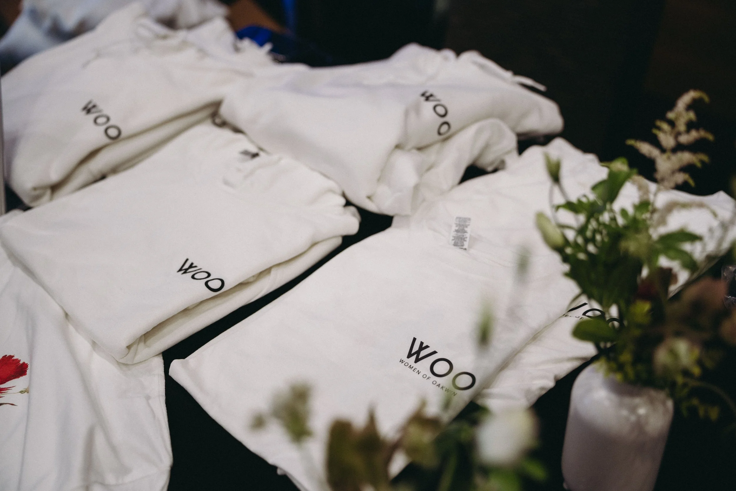 Several white cloth bags with black text that says 'Women of Oakwood' placed on a dark surface, with some green plants in the foreground.