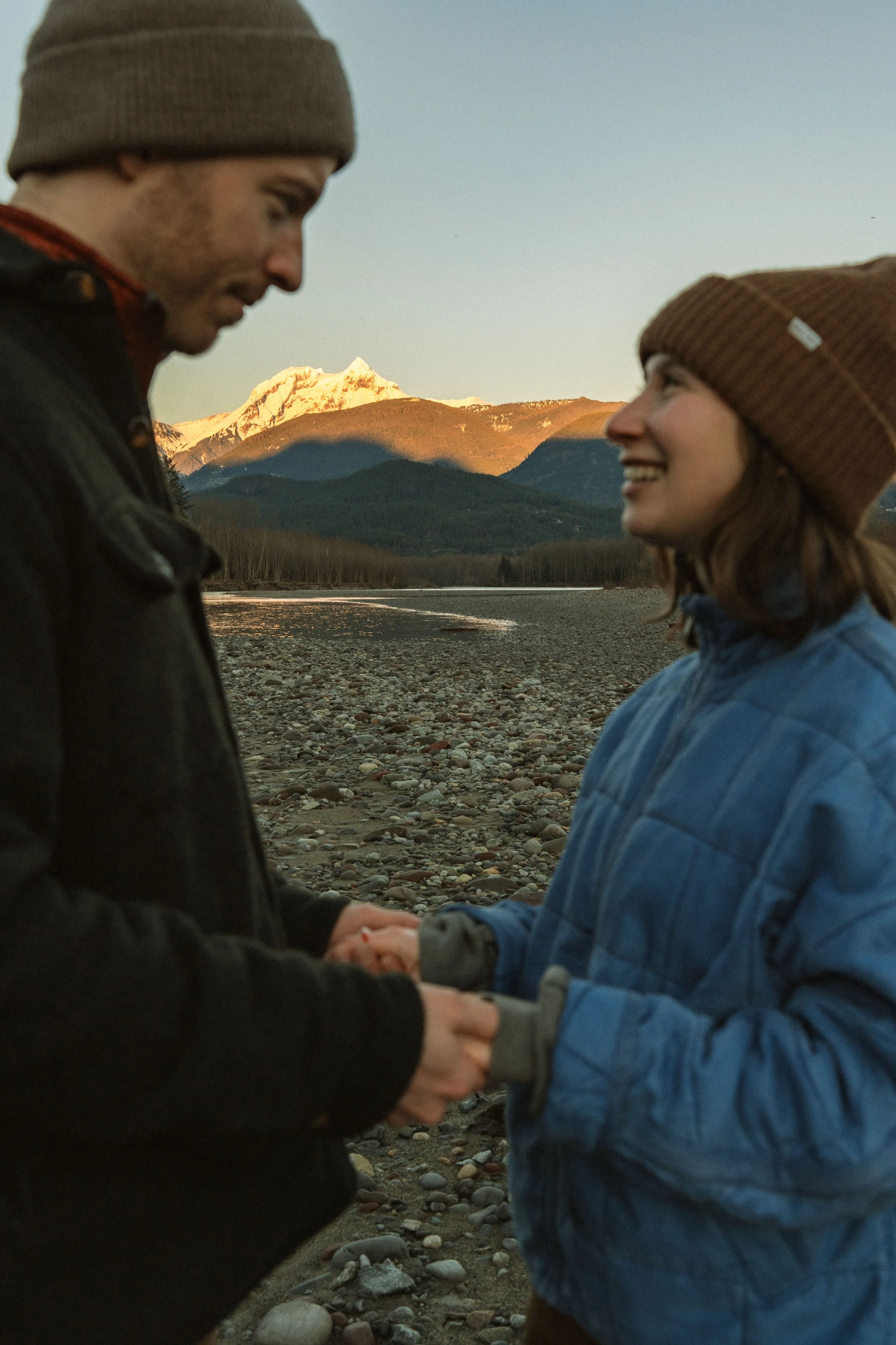 A man and woman holding hands in a scenic outdoor setting with mountains in the background.