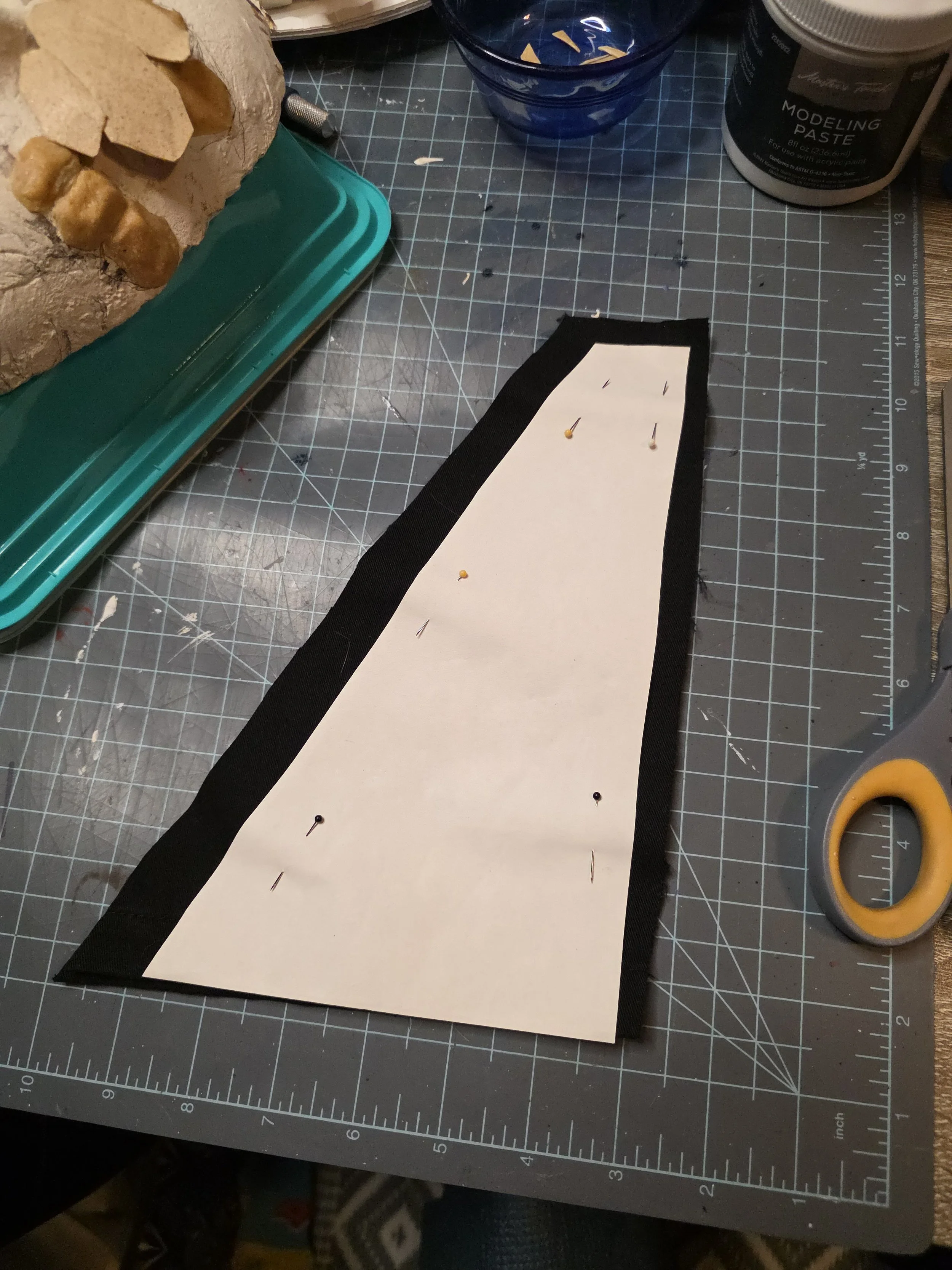 A paper triangle template pinned onto black fabric that has been cut our around it, with a half inch seam allowance.