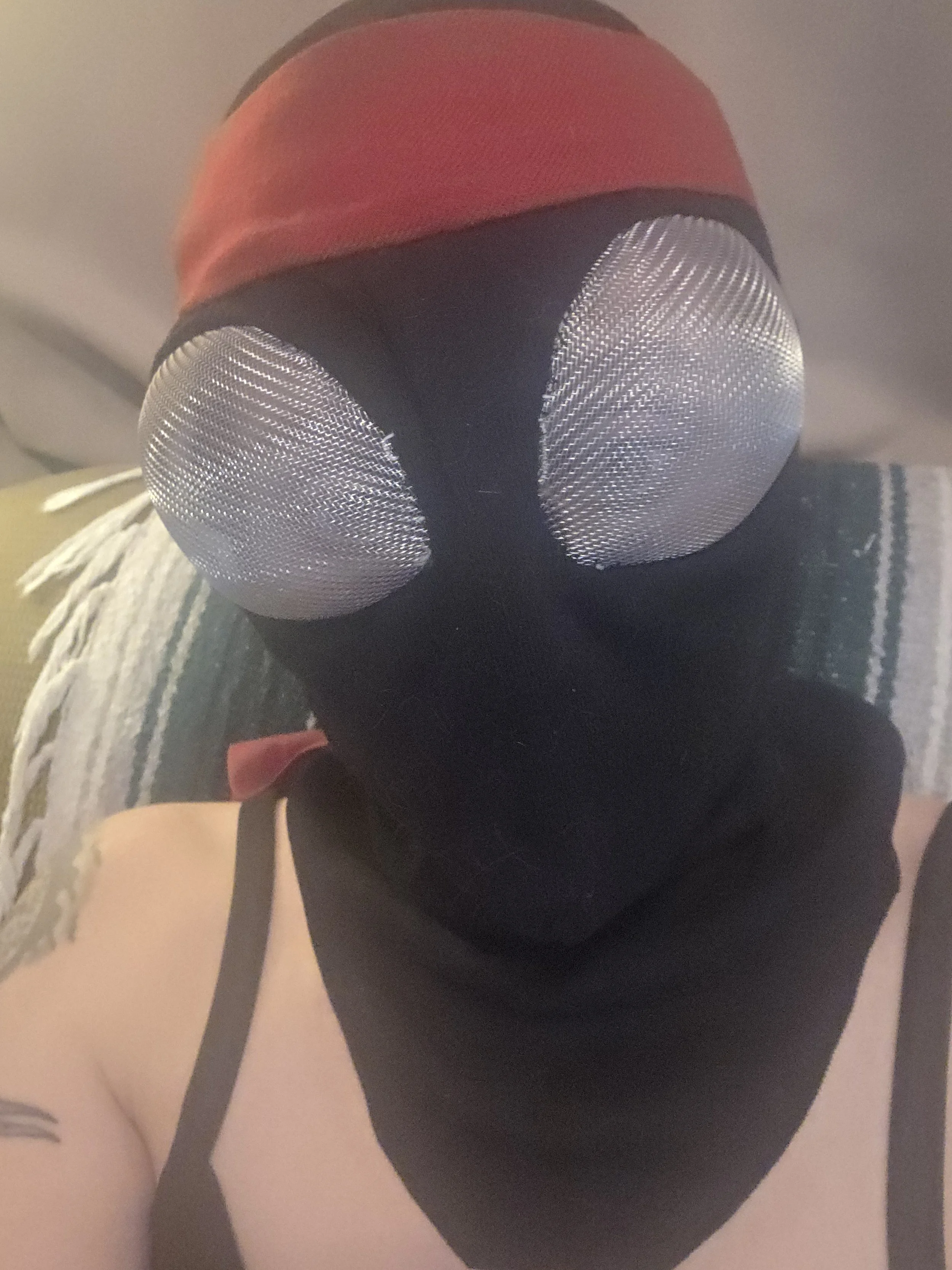 Person wearing a black ninja hood with bug-like metal mesh eye covers and a red headband