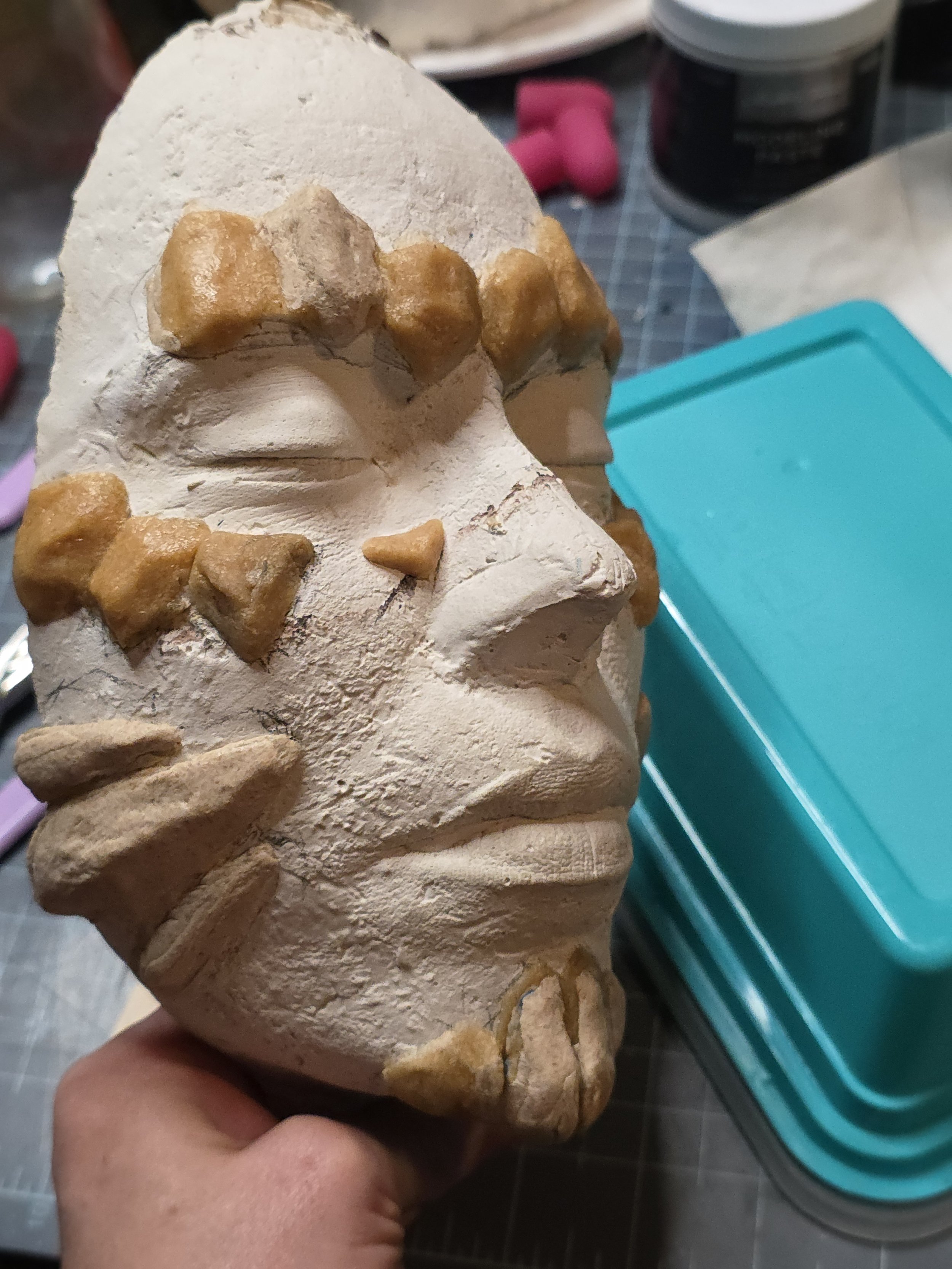 3/4 view of plaster face cast with rocklike scales made of tan worbla, placed over the eyebrows, cheekbones, chin, and jawline