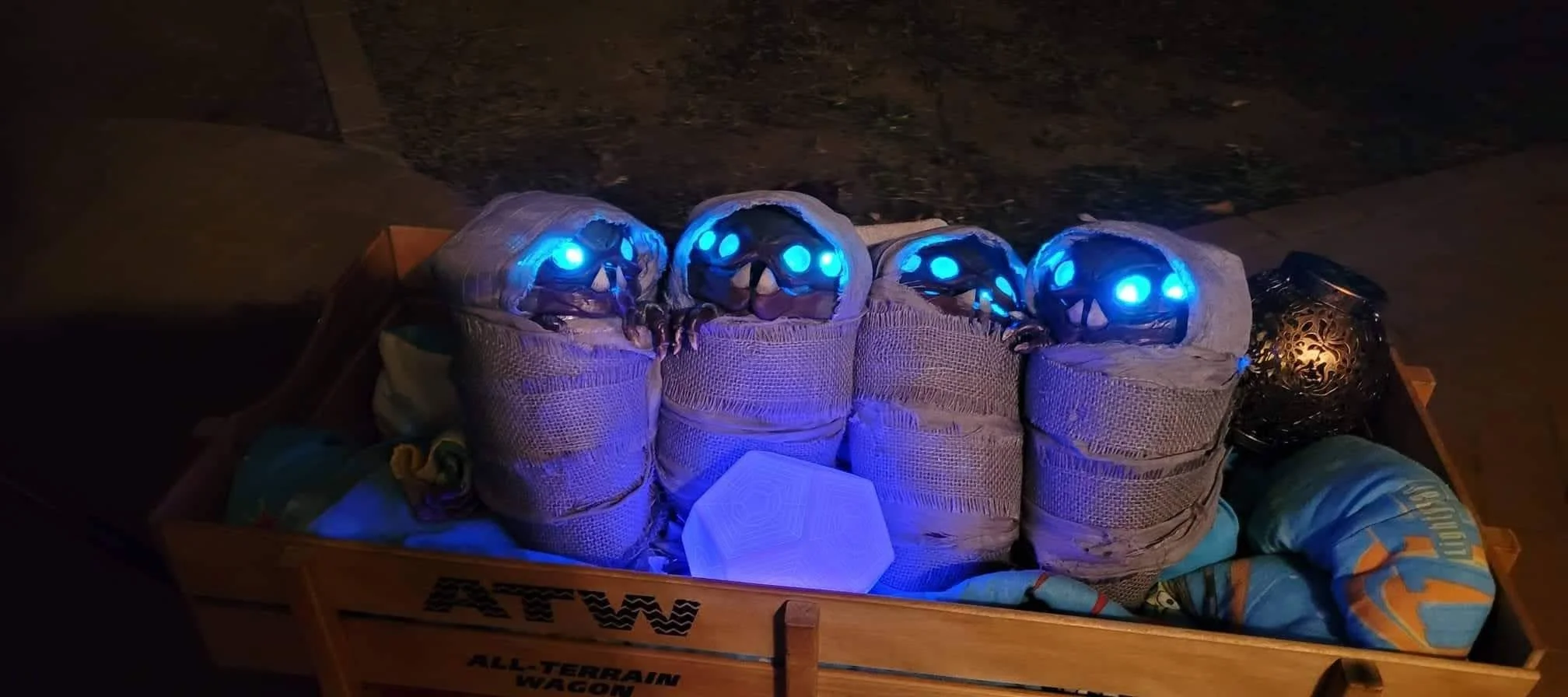 4 Buglike alien babies swaddled in light gray cloth. Each has 4 glowing blue eye and 2 pointy bottom teeth. 