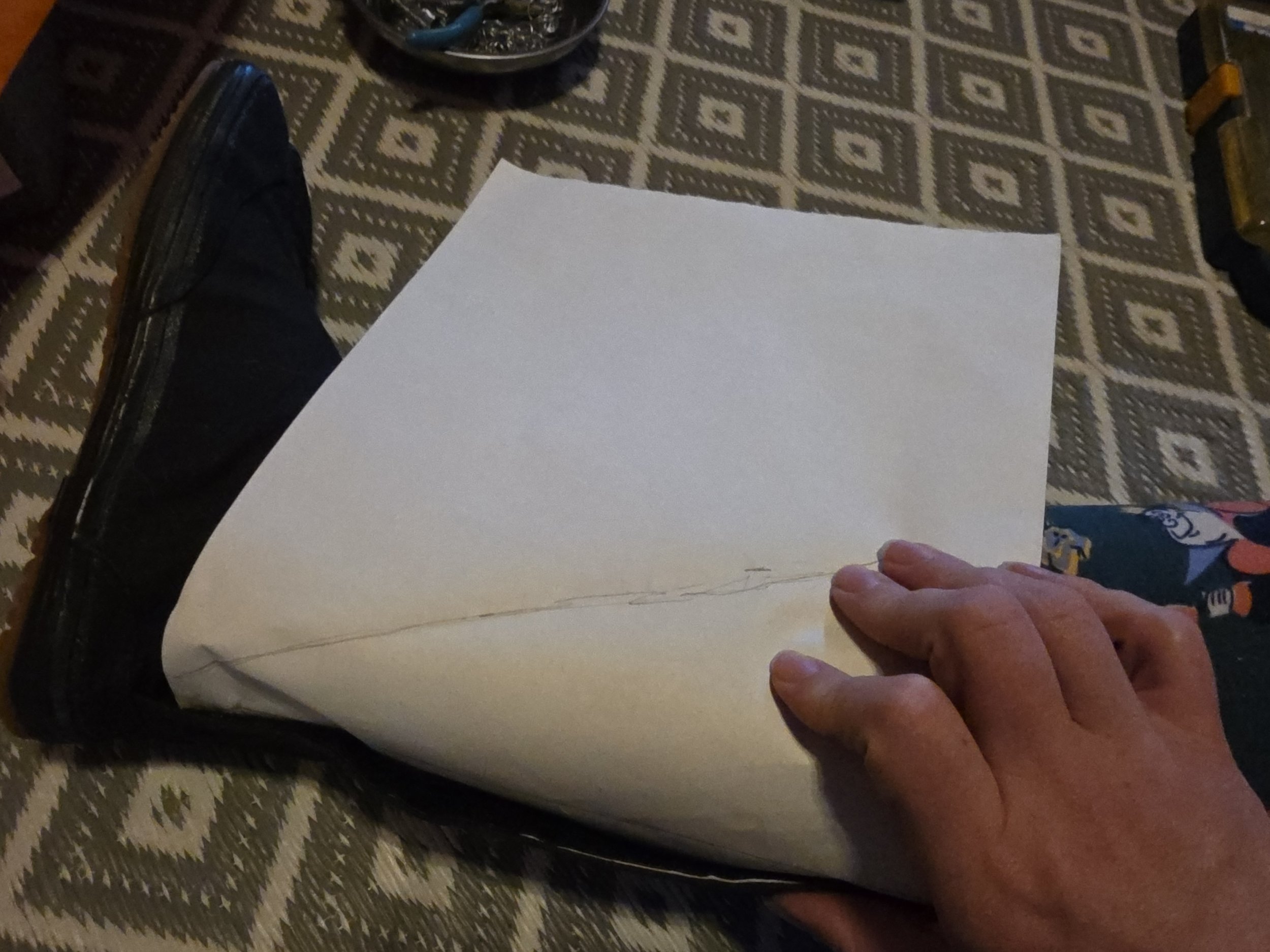 A foot in a black canvas boot that is too small to velcro closed. There is a piece of paper placed in the gap and the triangular shape of the gap is traced on the paper