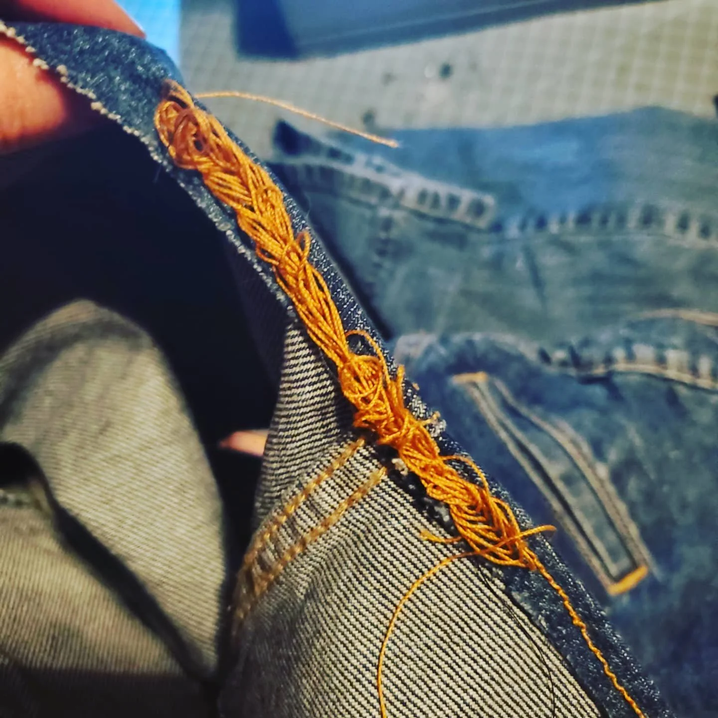 closeup of some badly tangled yellow thread on a denim seam, where the sewing machine jammed